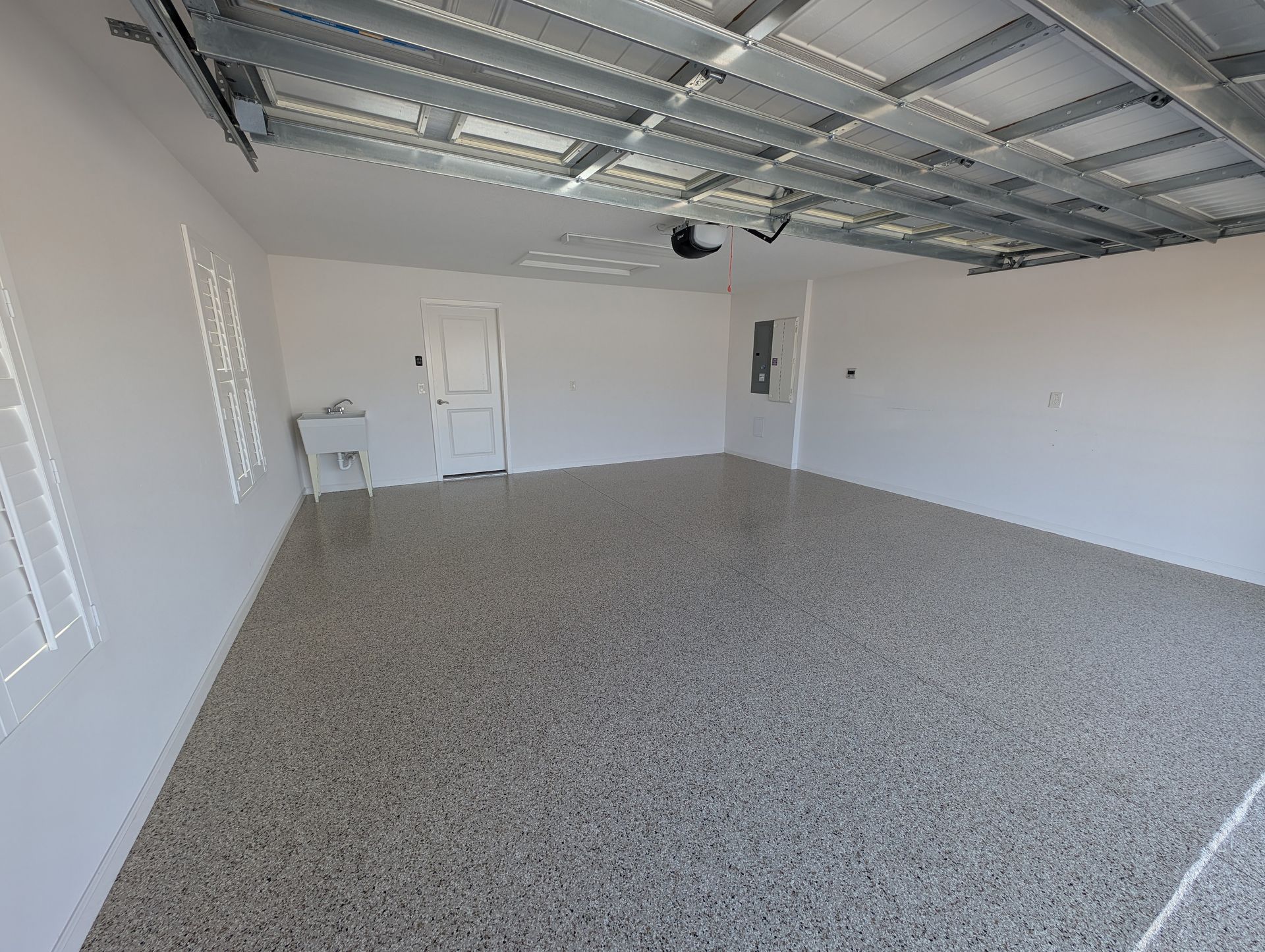 Empty garage with white walls, speckled floor, and exposed metal ceiling.