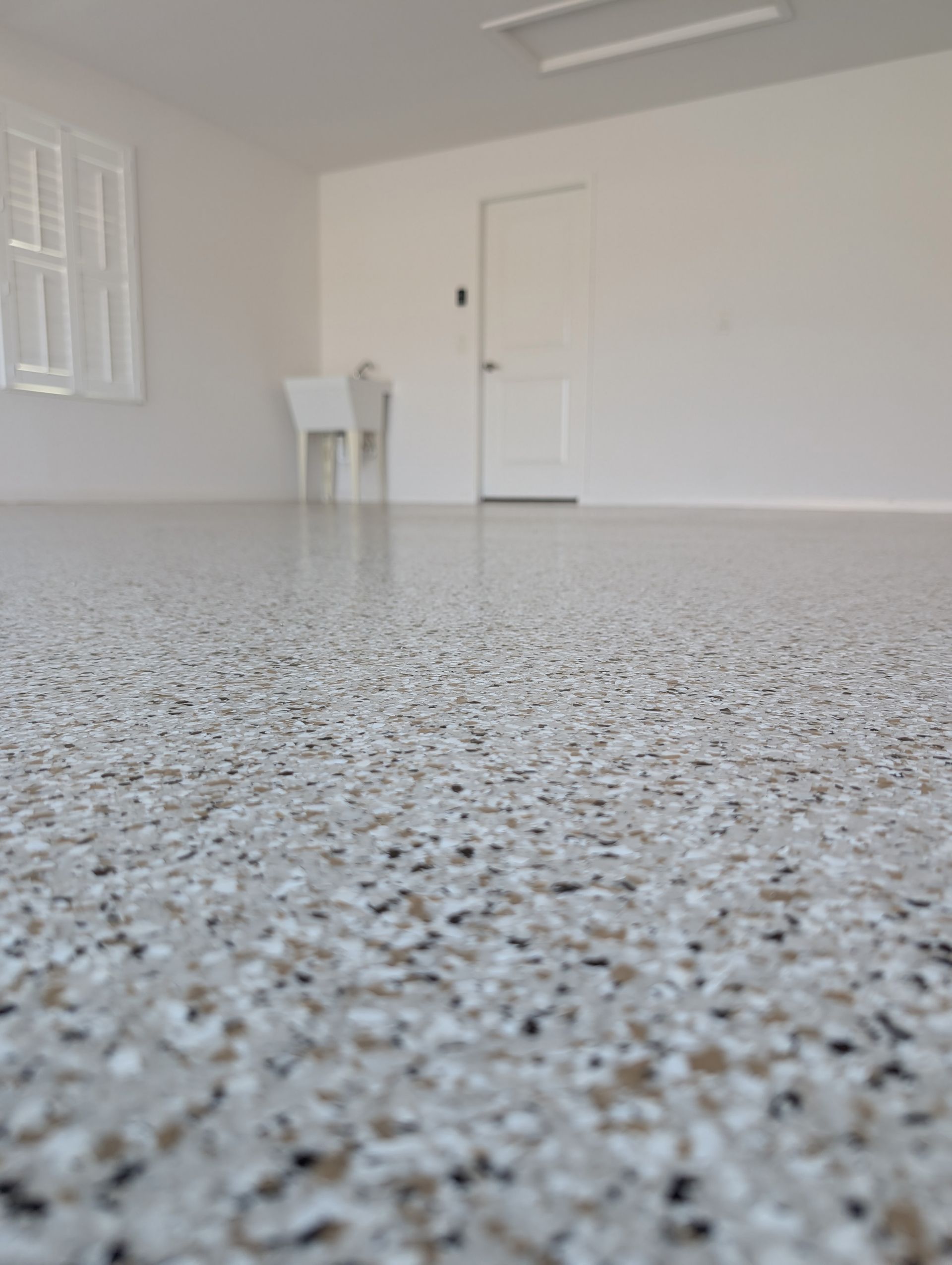 Empty white room with speckled gray floor, small white table, and a closed door.