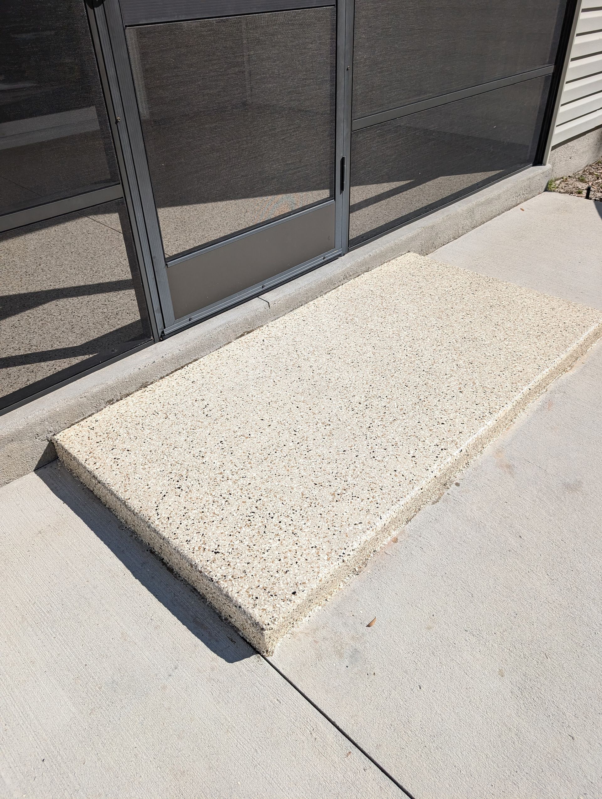 Light concrete ramp beside a dark metal gate, meeting a sidewalk at the entrance.