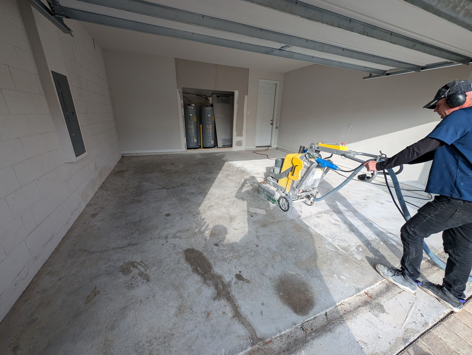 Worker power-troweling a concrete floor inside a garage under construction.