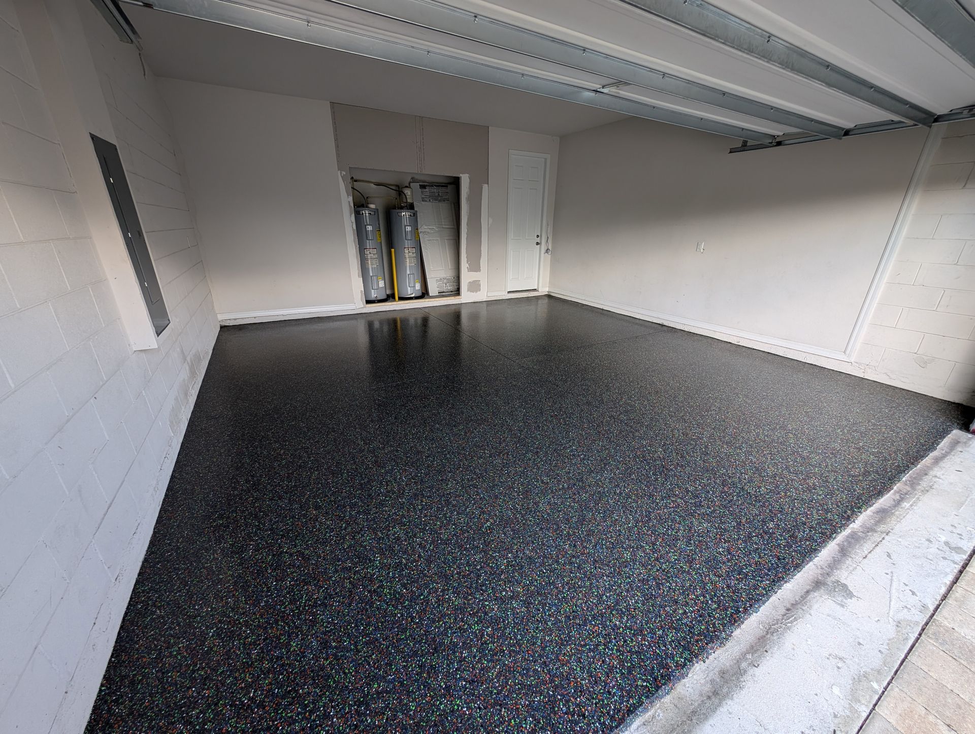 Empty garage with black speckled floor and open overhead door, showing exposed insulation at the back.