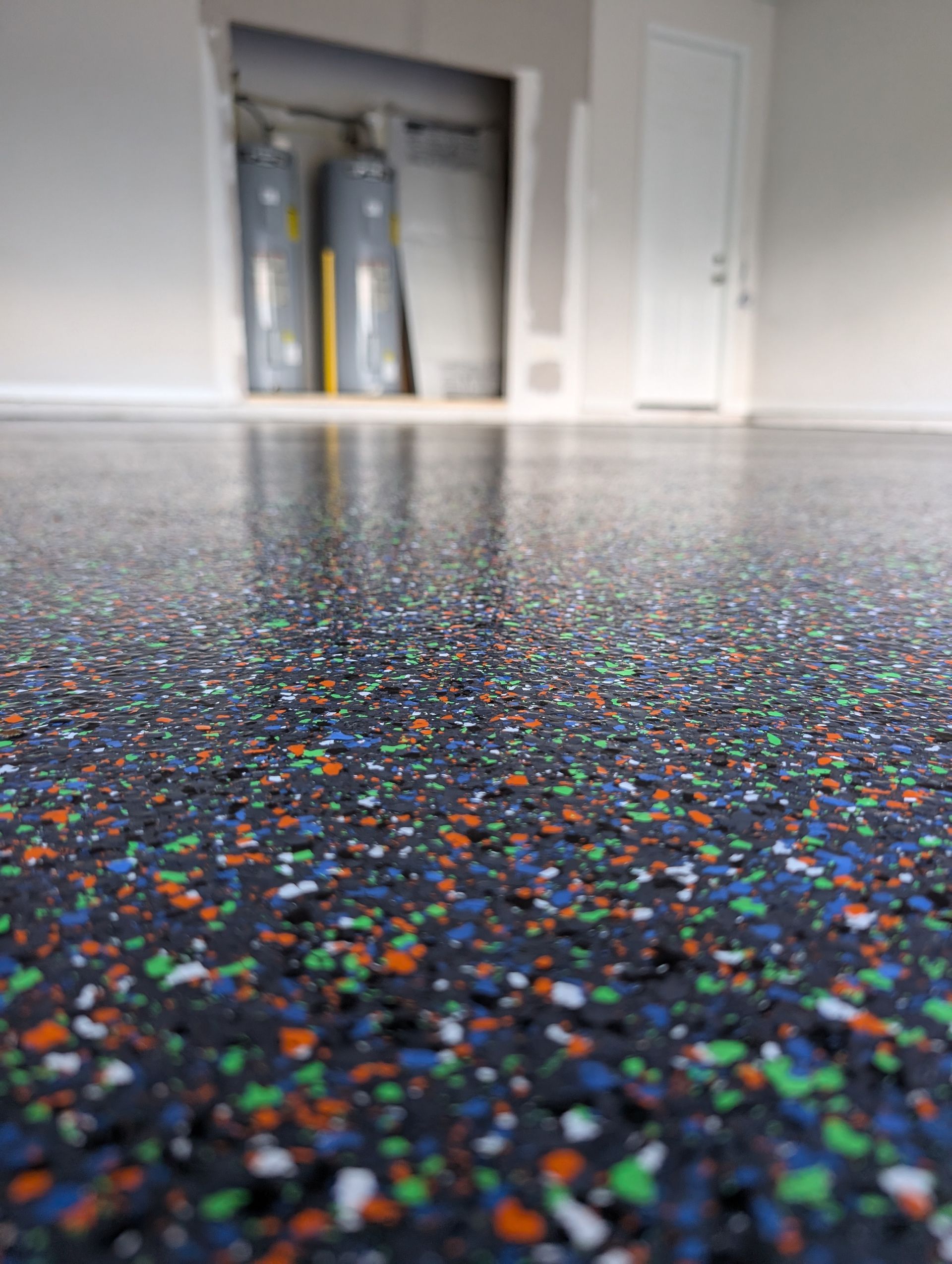 Colorful speckled epoxy floor in a garage, with cabinets and equipment in the background.
