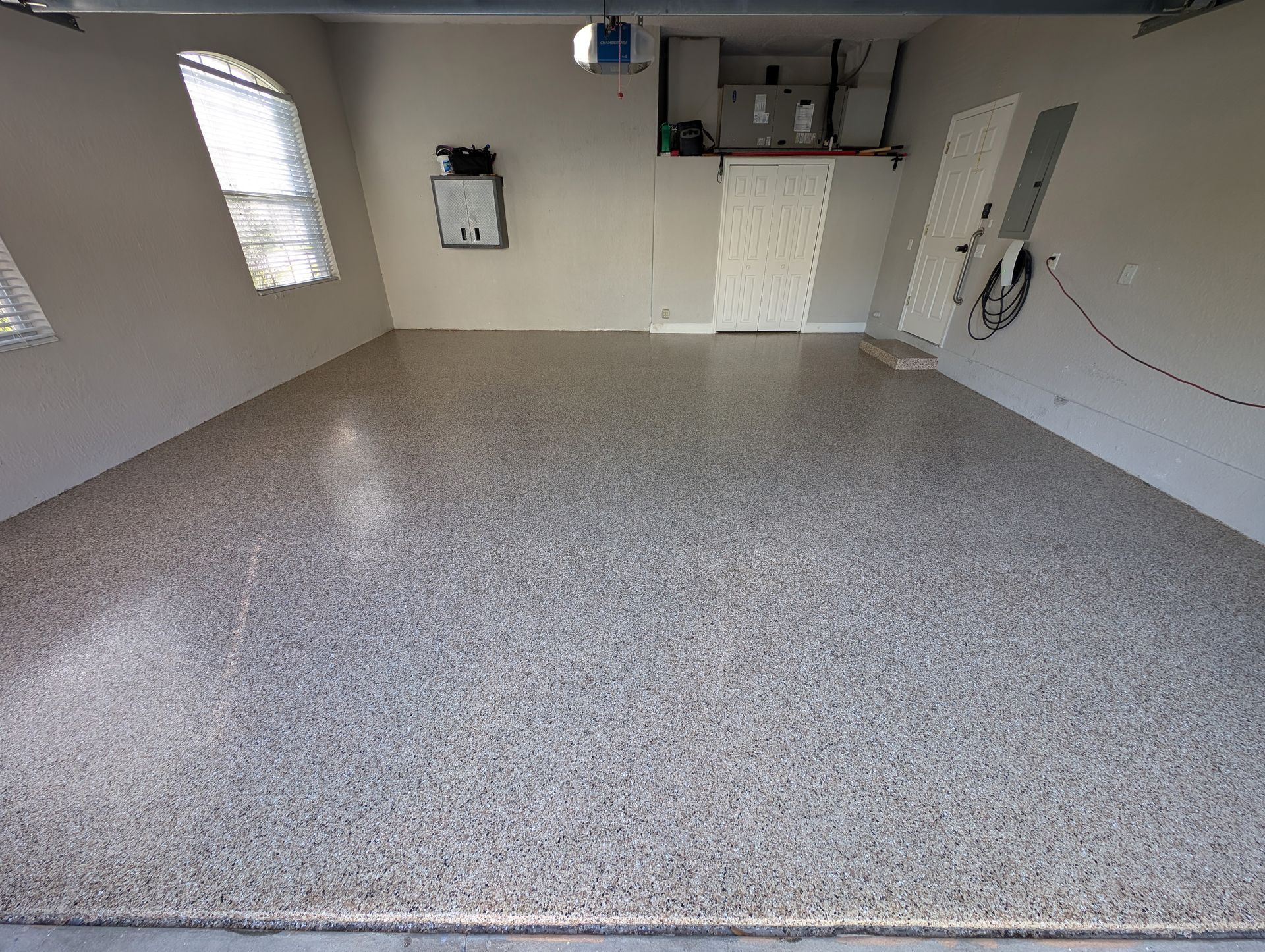 Empty garage with speckled epoxy floor and wall-mounted storage/cabinets.