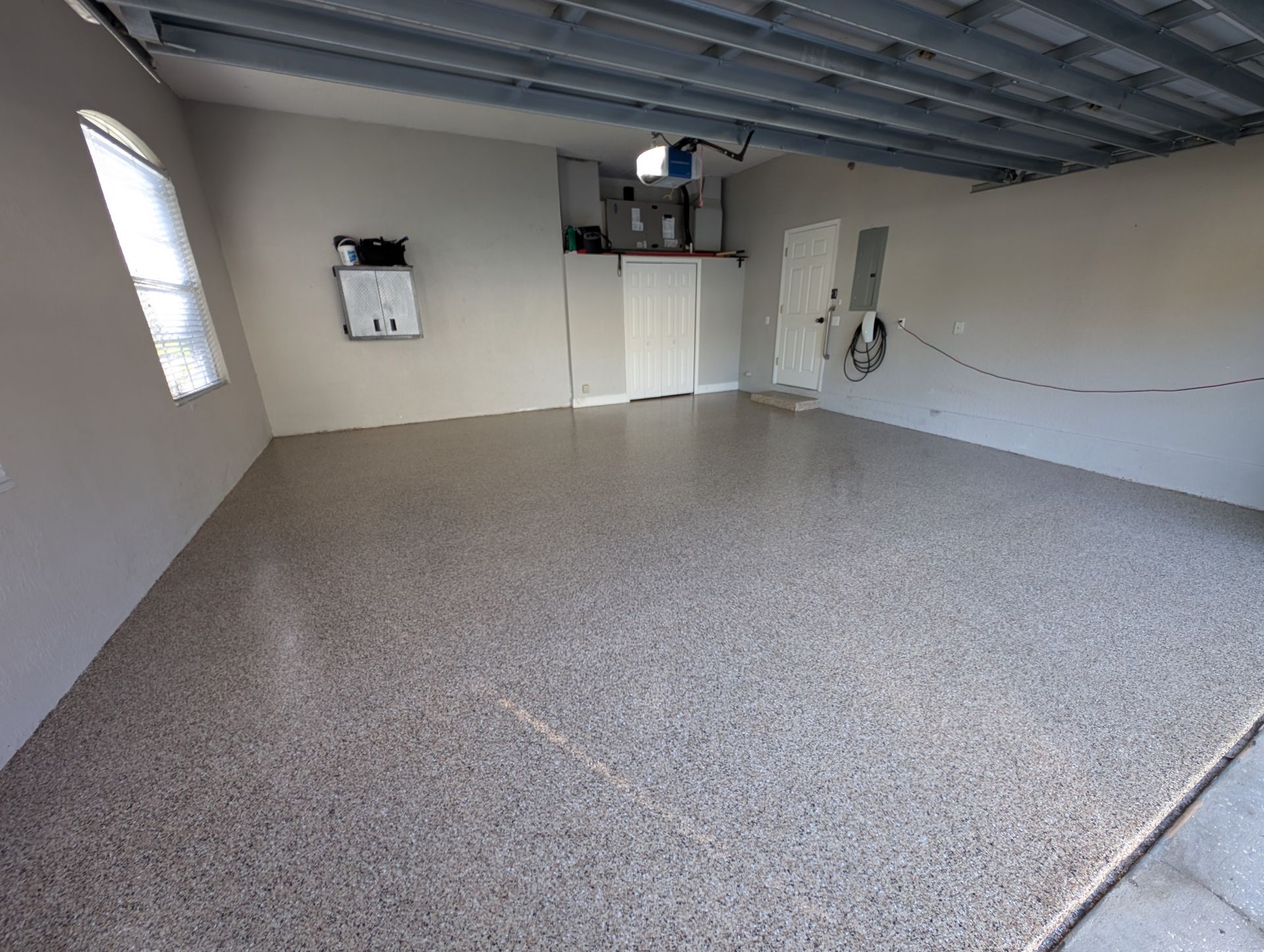 Empty garage with speckled epoxy floor, exposed ceiling, and utility fixtures on the walls.