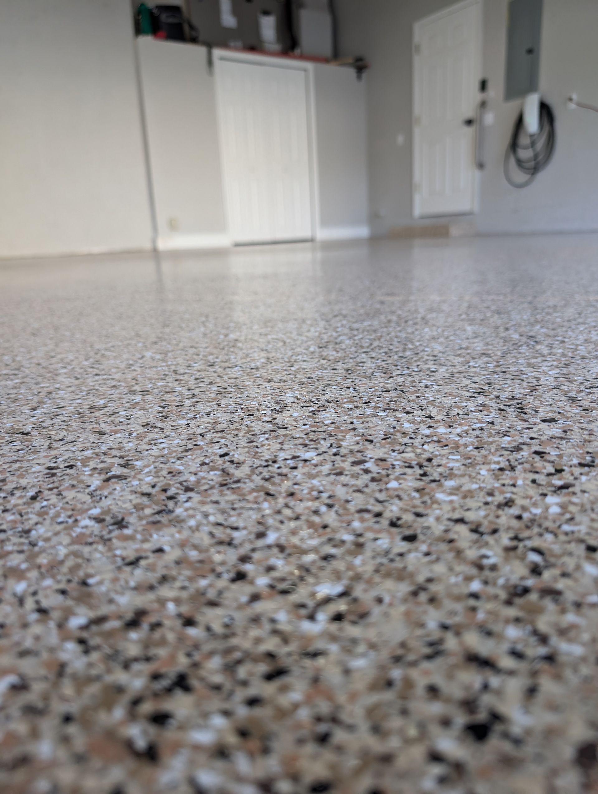 Close-up of speckled epoxy floor in a garage-like room with cabinets and wall-mounted tools in the background