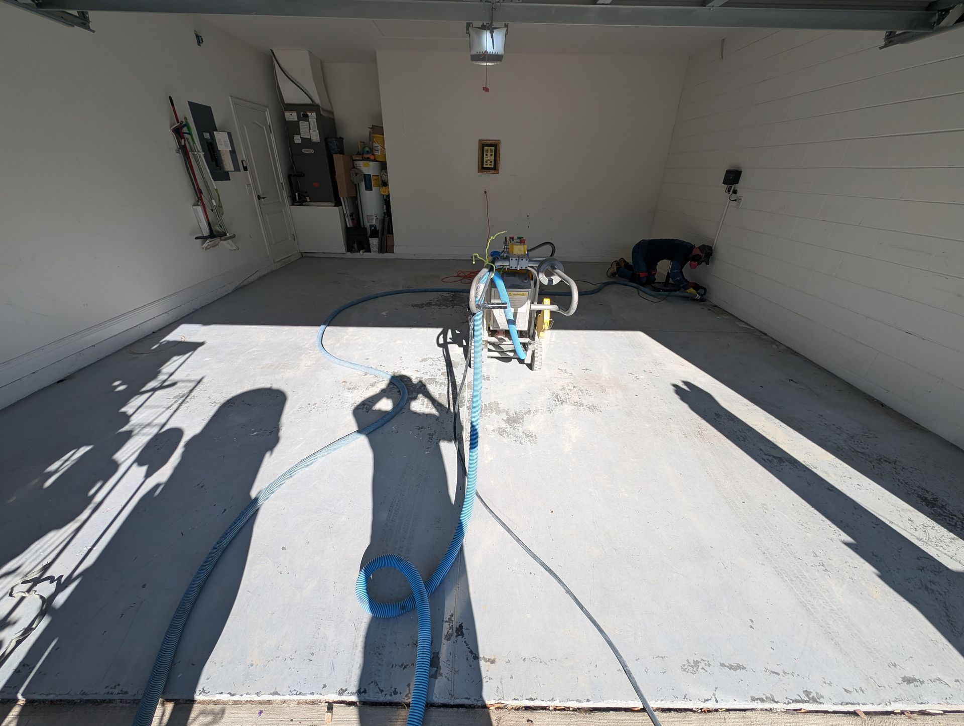 Garage interior with a concrete floor, a work cart in the center, and long shadows from the open doorway.
