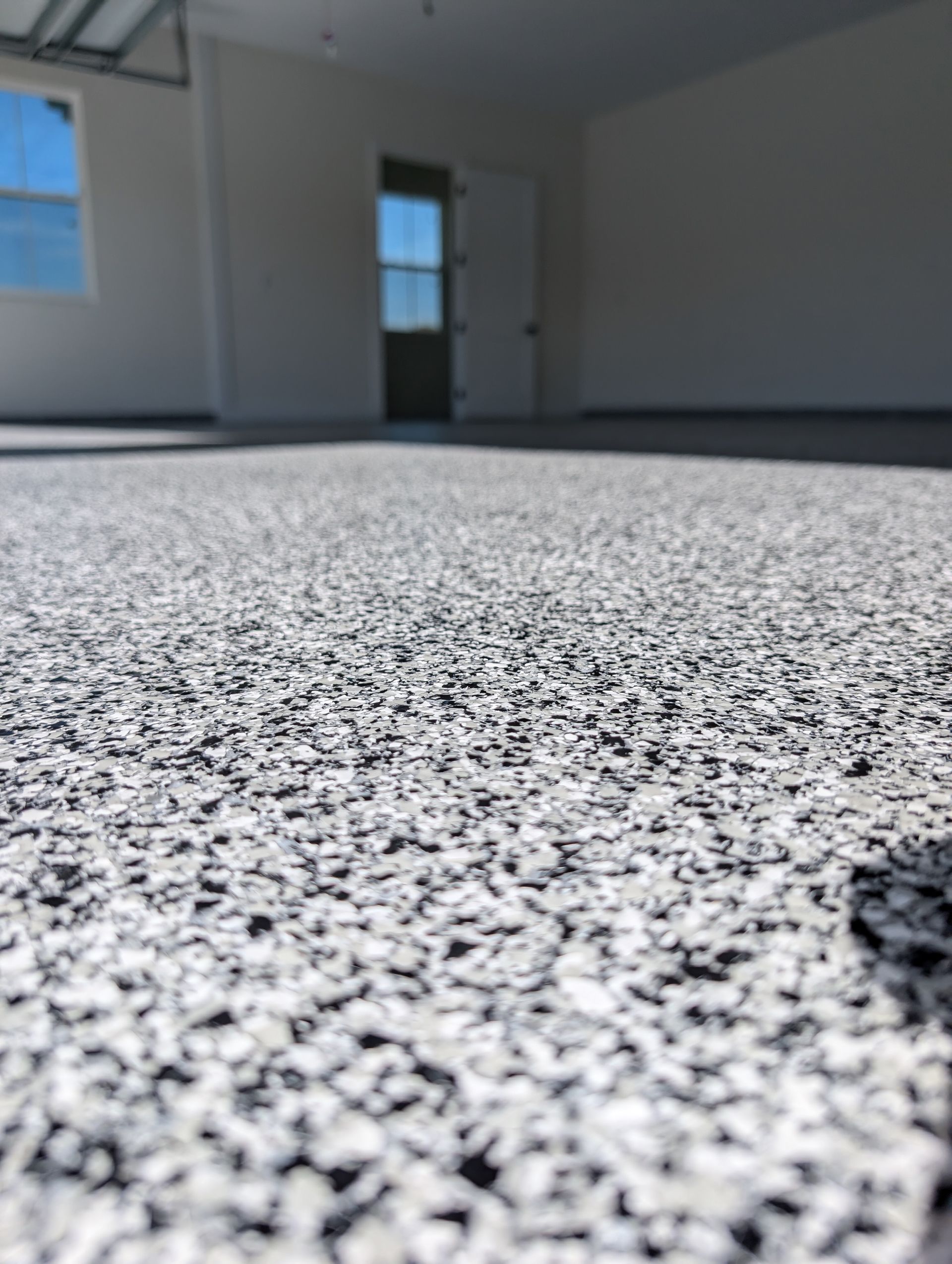 Low-angle view of a speckled floor in a bright empty room with windows and a door.