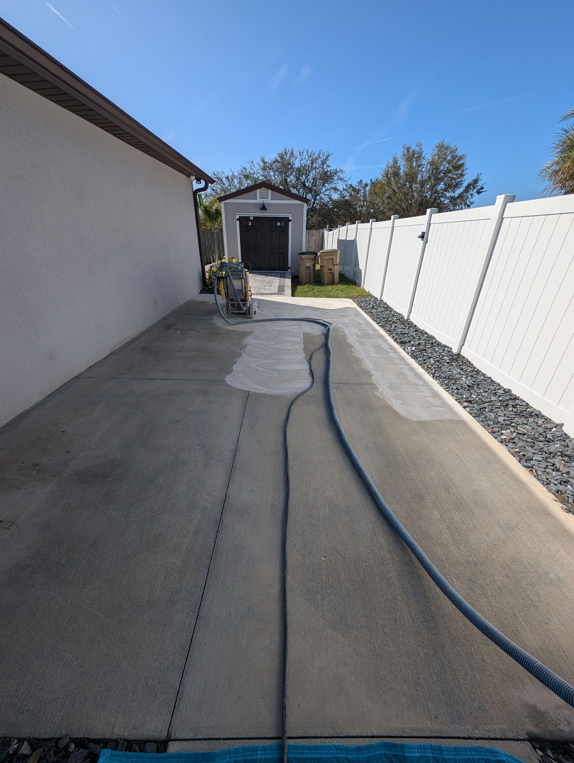 Narrow concrete driveway beside a white fence, with a garden shed at the far end.