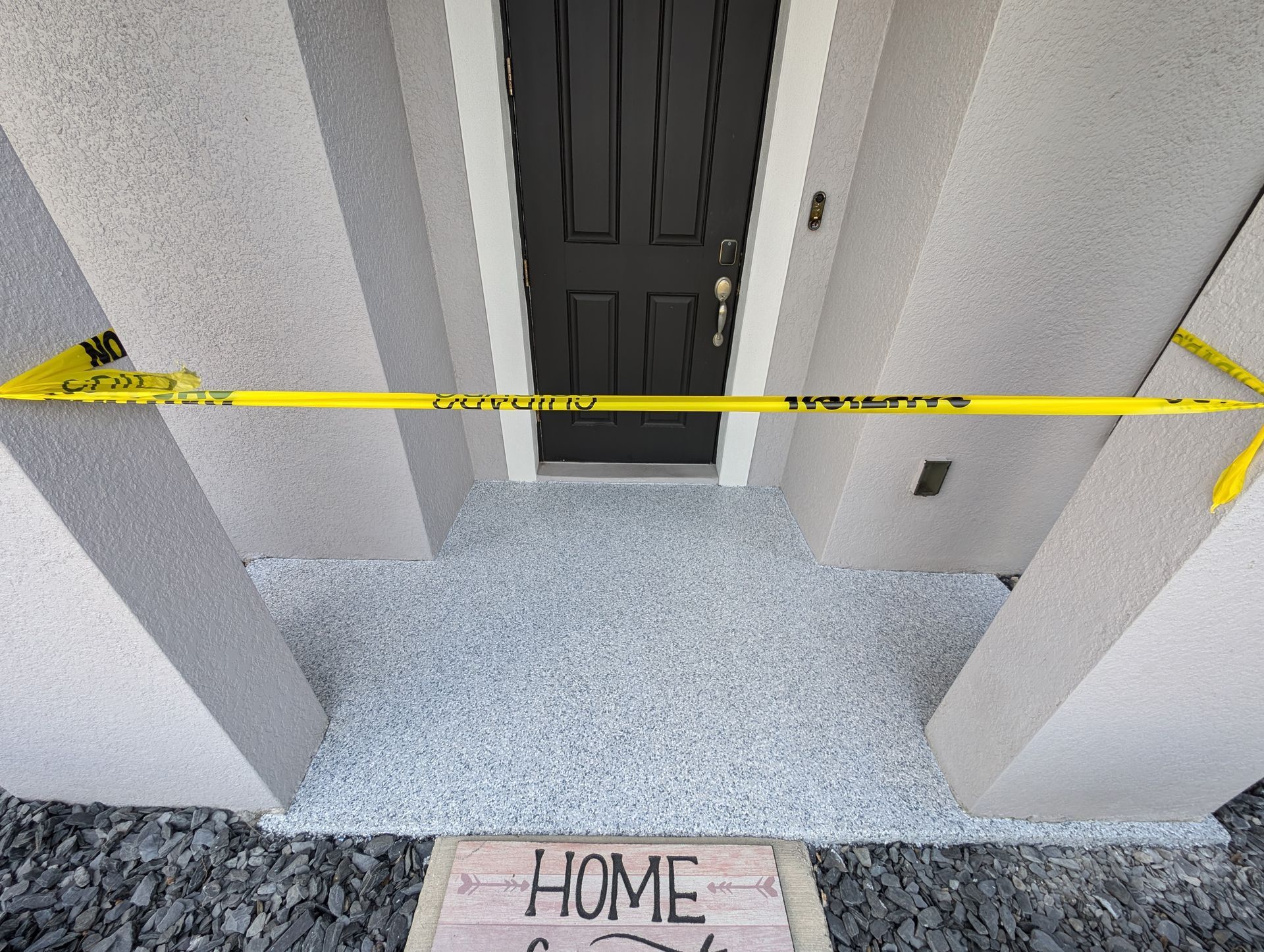 Front porch with yellow caution tape blocking a black front door and a HOME doormat