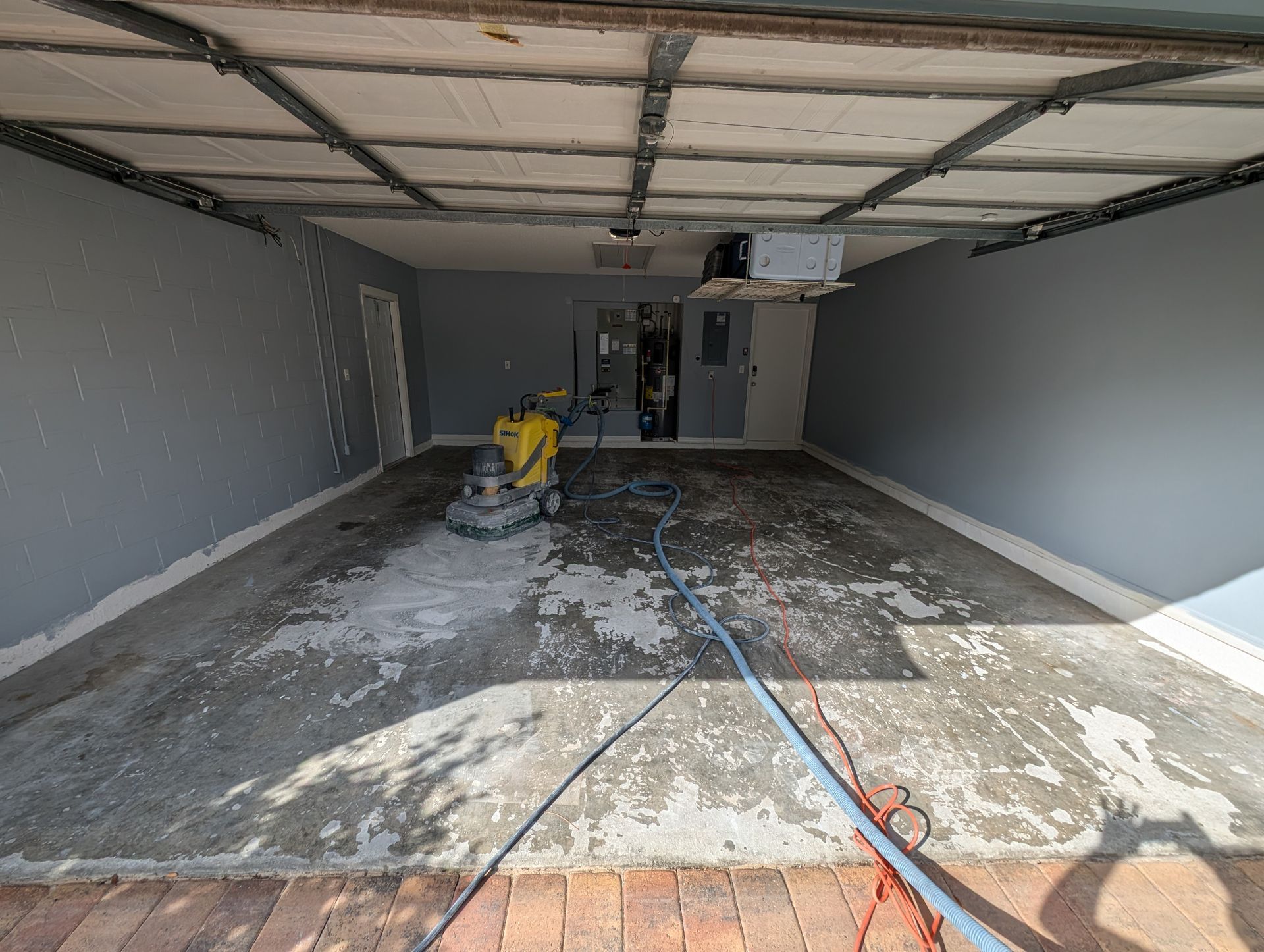 Empty garage under construction with dusty concrete floor, tools, and a yellow floor grinder.