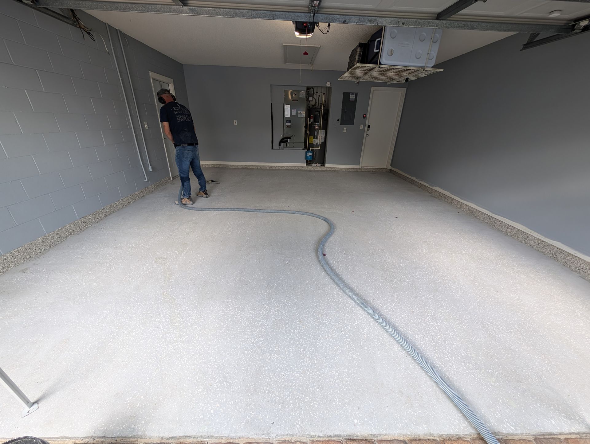 Empty unfinished room with gray walls, white floor, and two workers installing overhead fixtures.