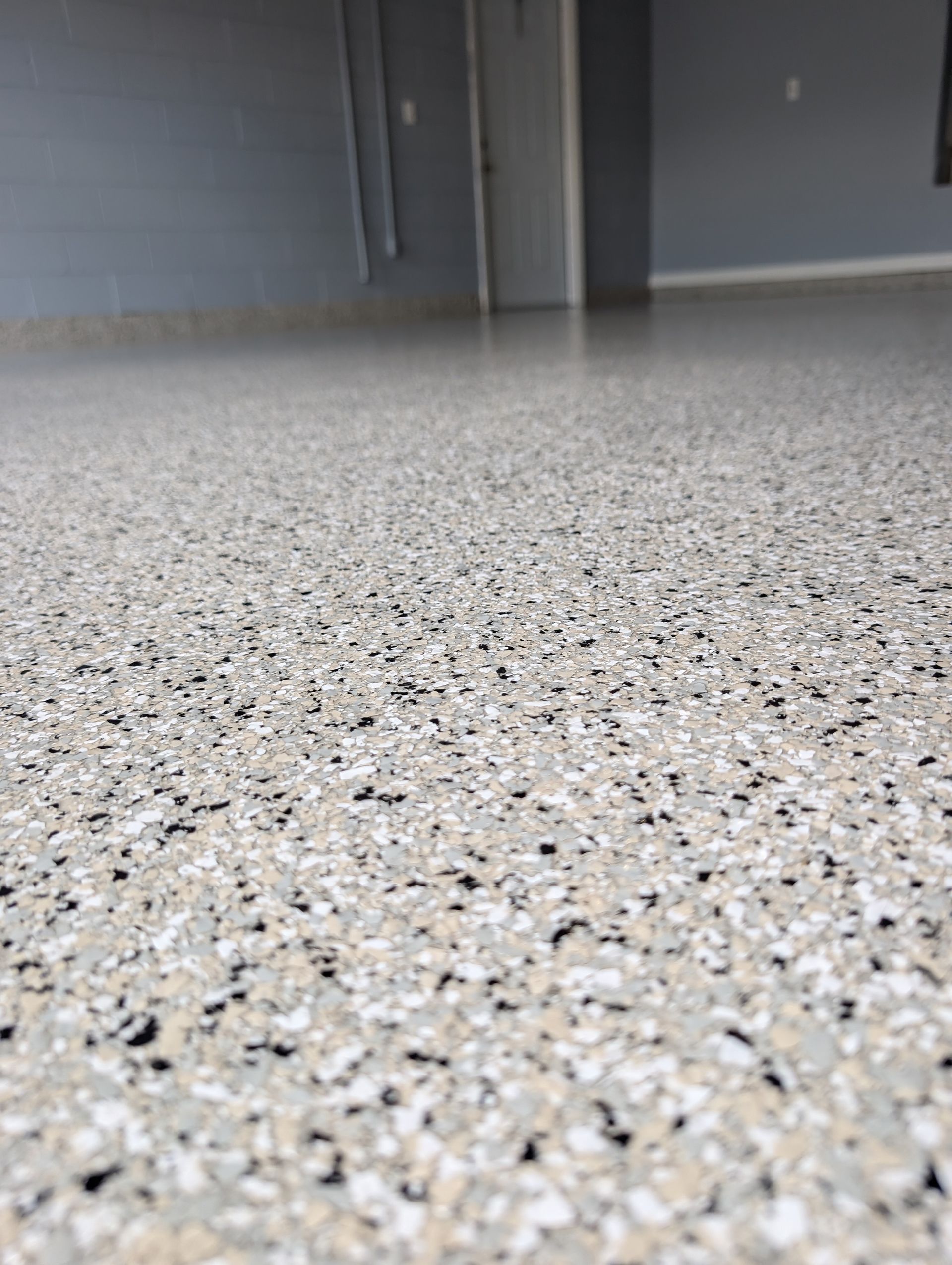 Close-up of a speckled epoxy floor in a gray indoor room with closed doors in the background