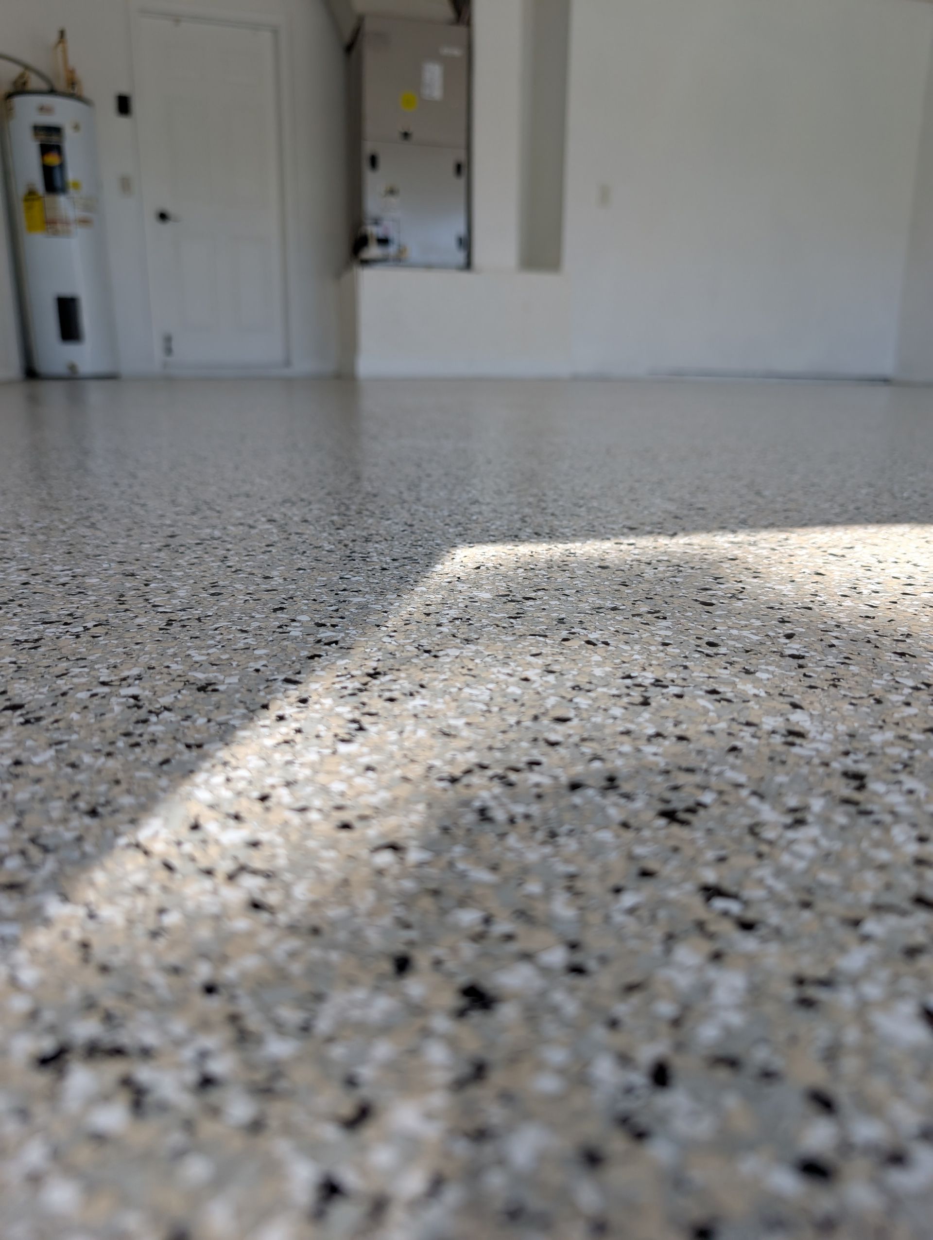 Speckled terrazzo floor in a bright empty room, with sunlight casting a diagonal shadow.