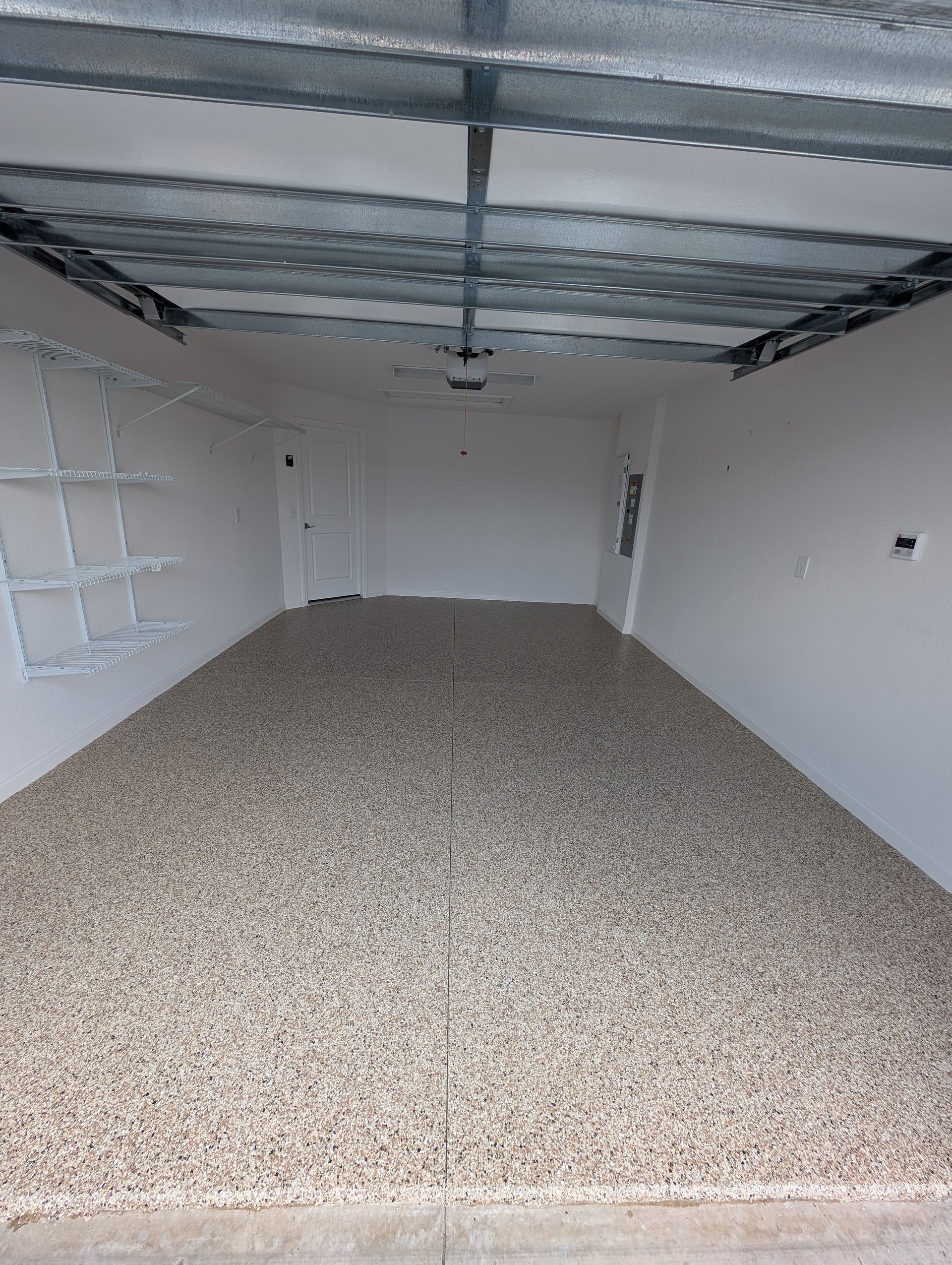 Empty garage with gravel floor, white walls, and open ceiling beams.