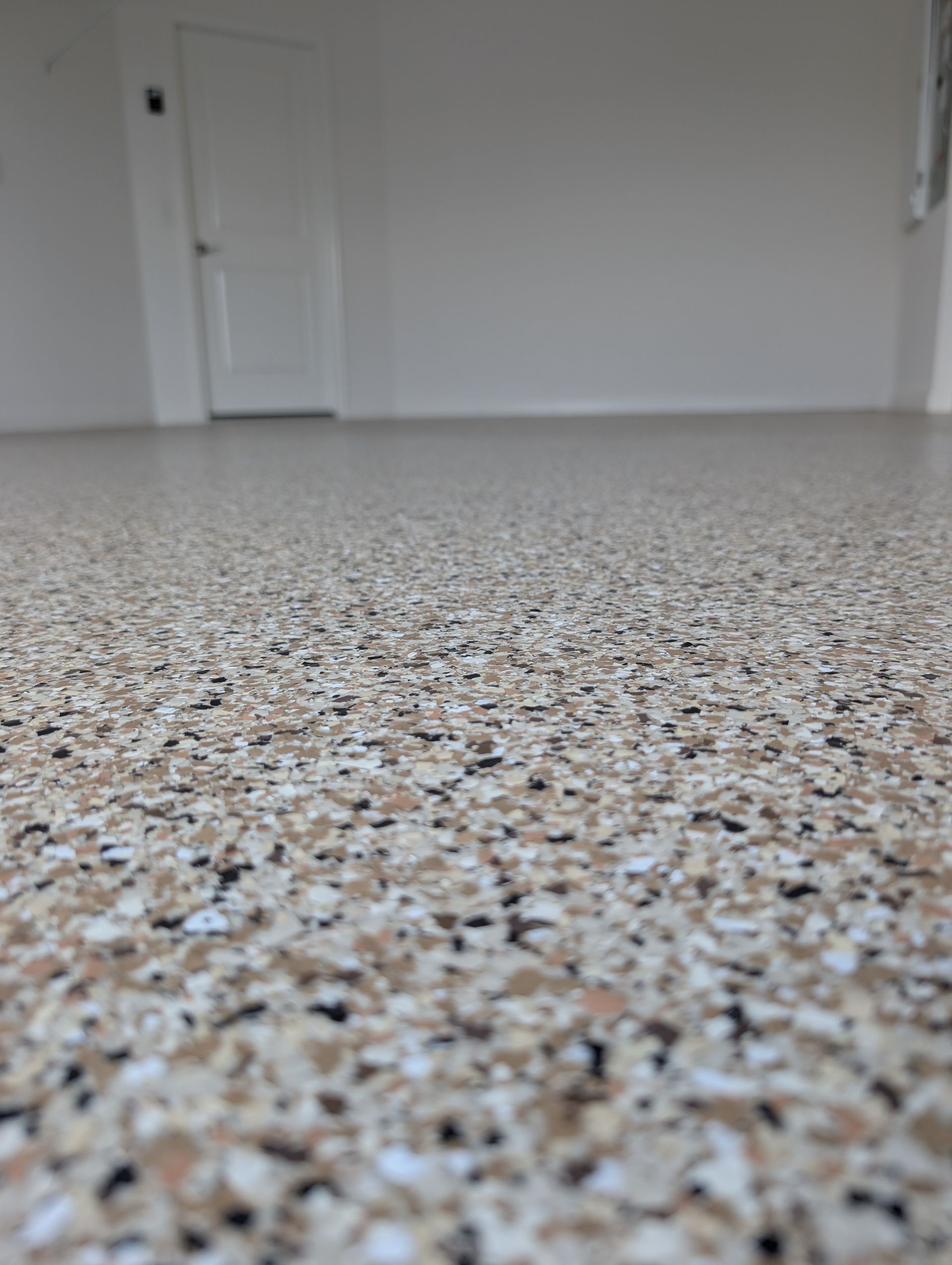 Close-up of speckled terrazzo floor in an empty white room, with a closed door in the background