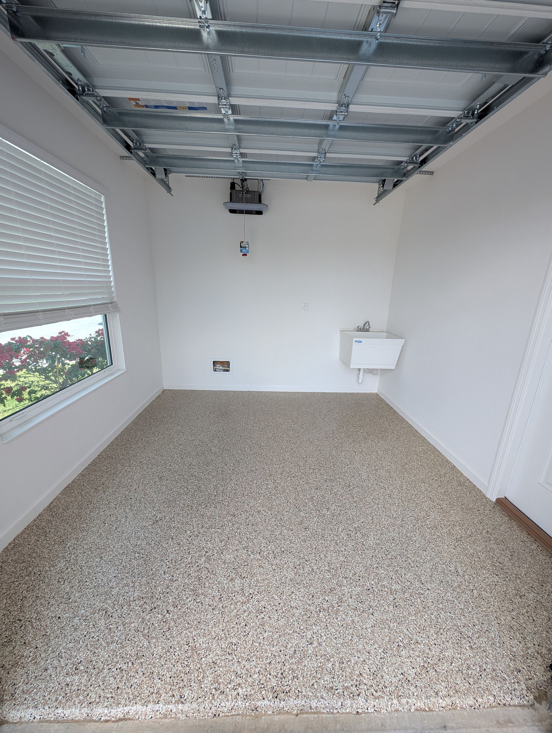 Empty room with speckled floor, white walls, exposed ceiling, window blinds, and a small sink on the right.