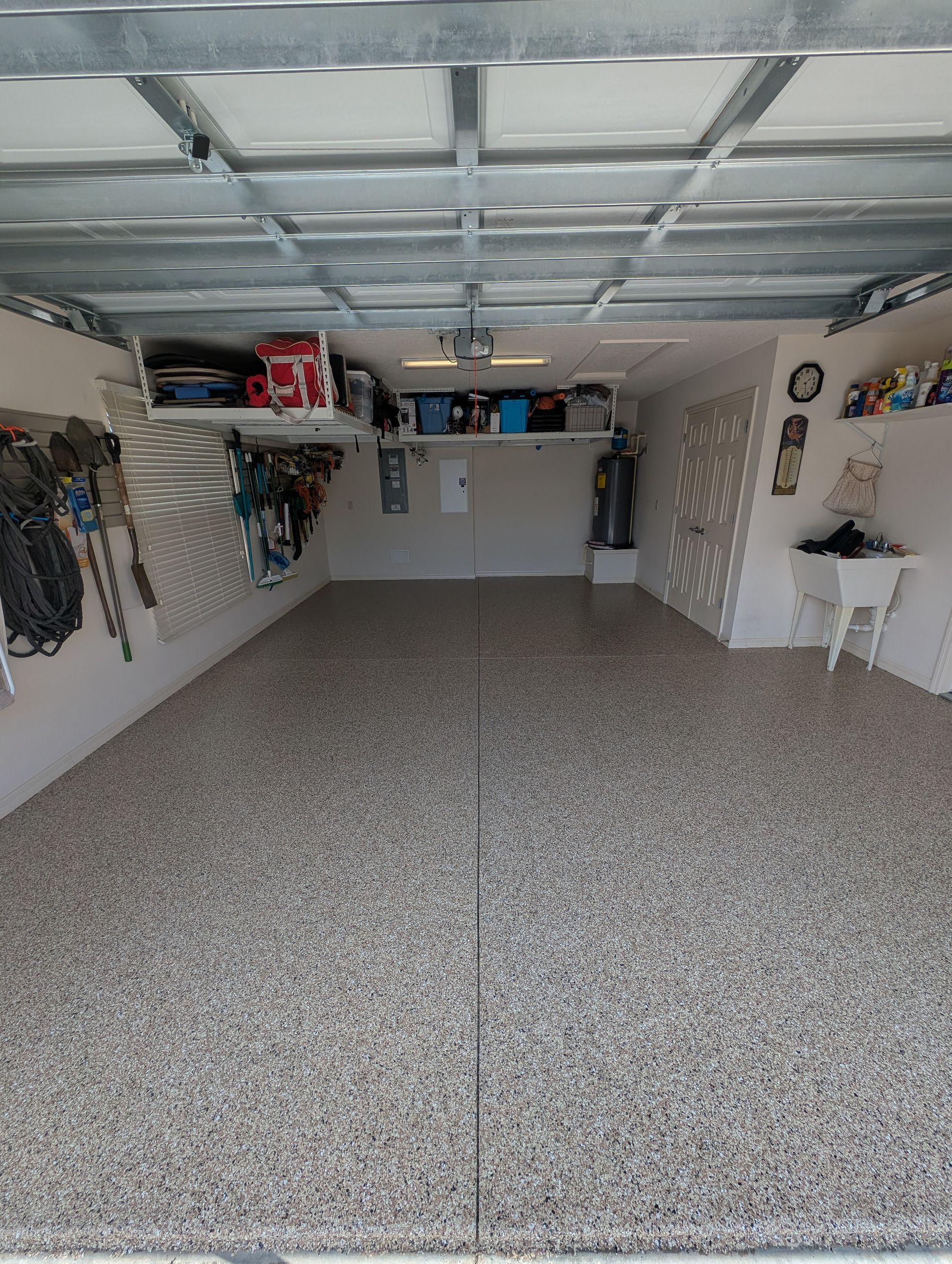 Empty garage with speckled floor, white walls, overhead storage, and a workbench at the back.
