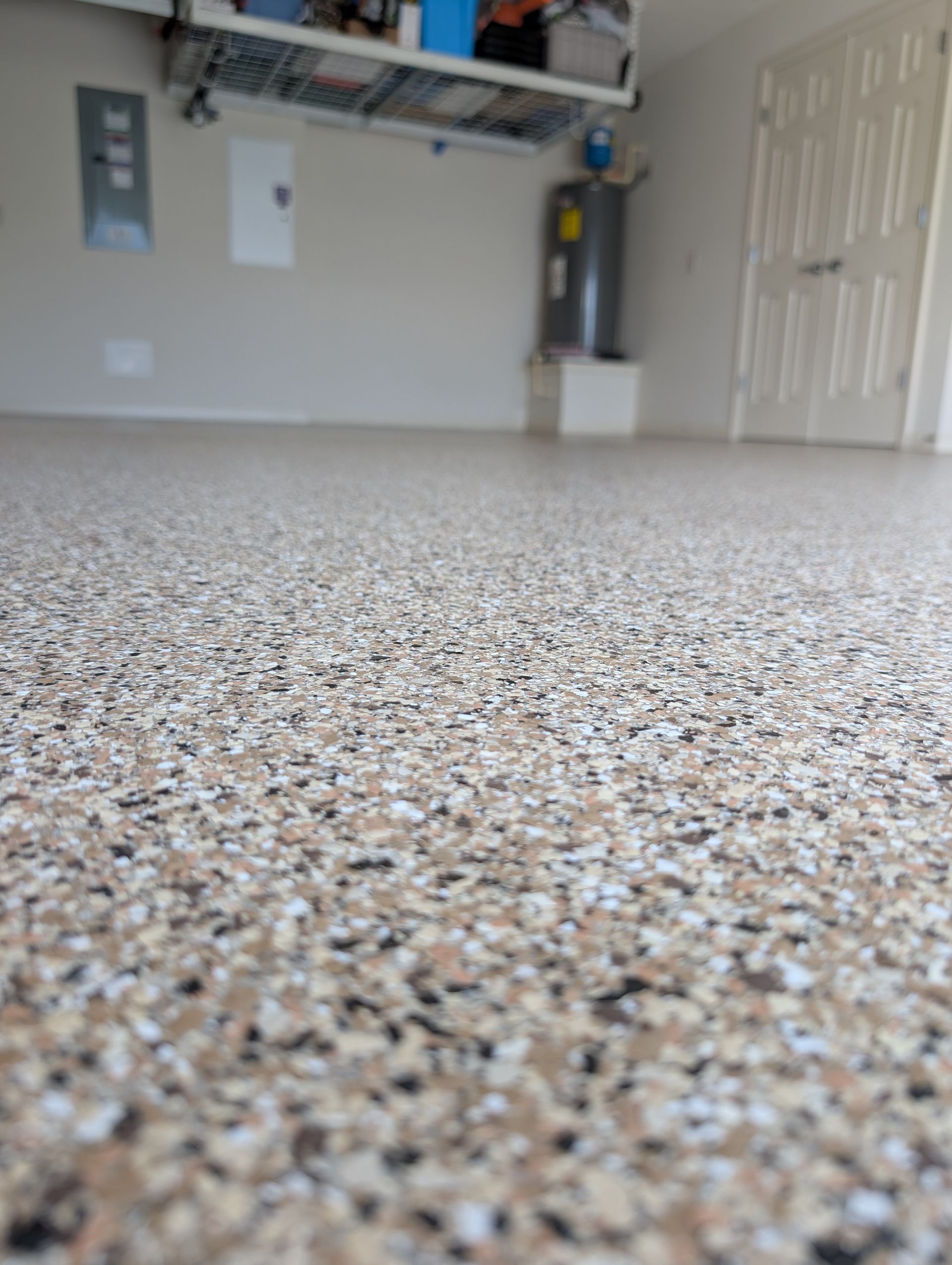 Low-angle view of a speckled garage floor with storage shelves and a white door in the background
