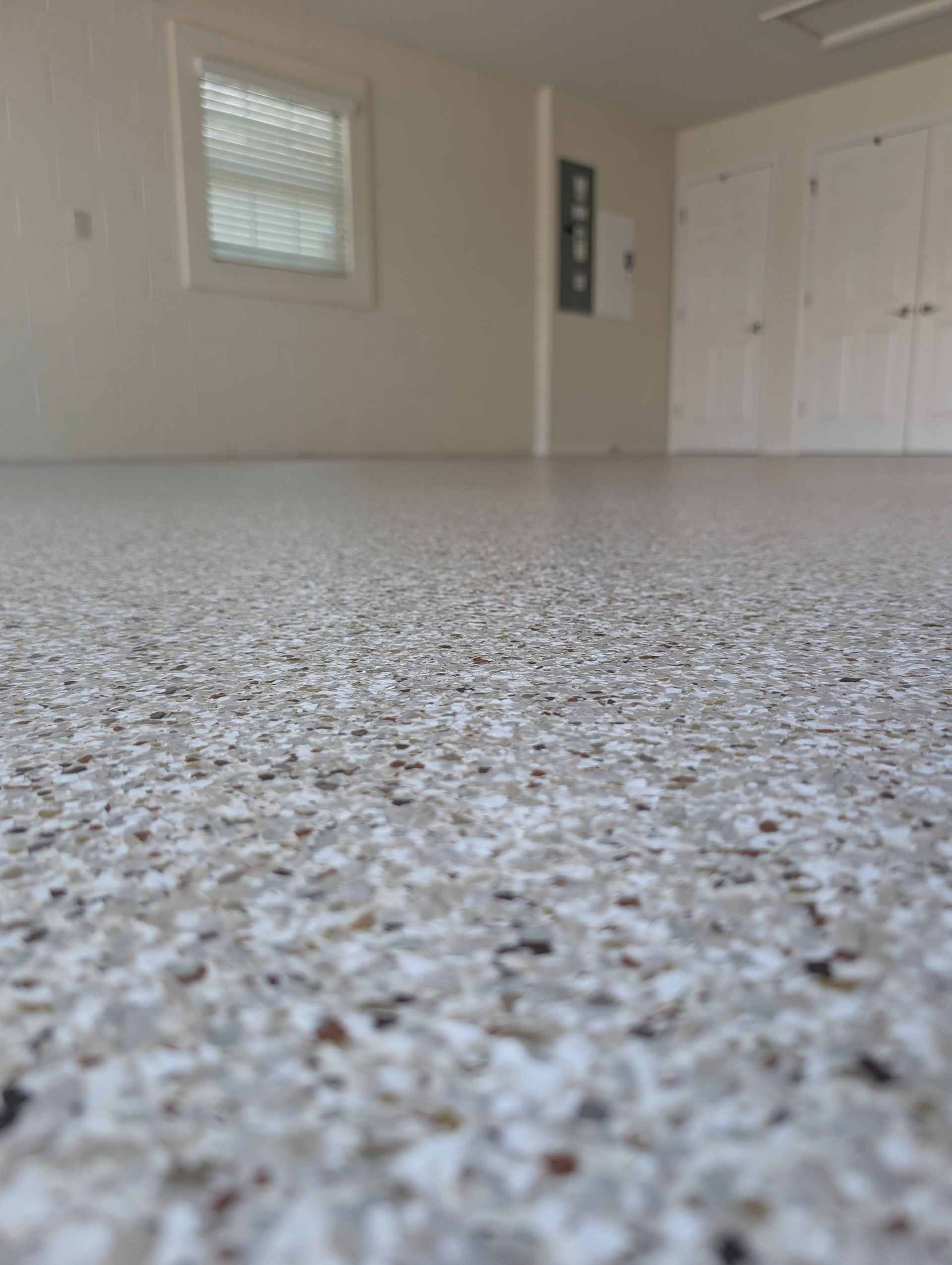 Empty garage with speckled floor, white walls, a window, and closed double doors.