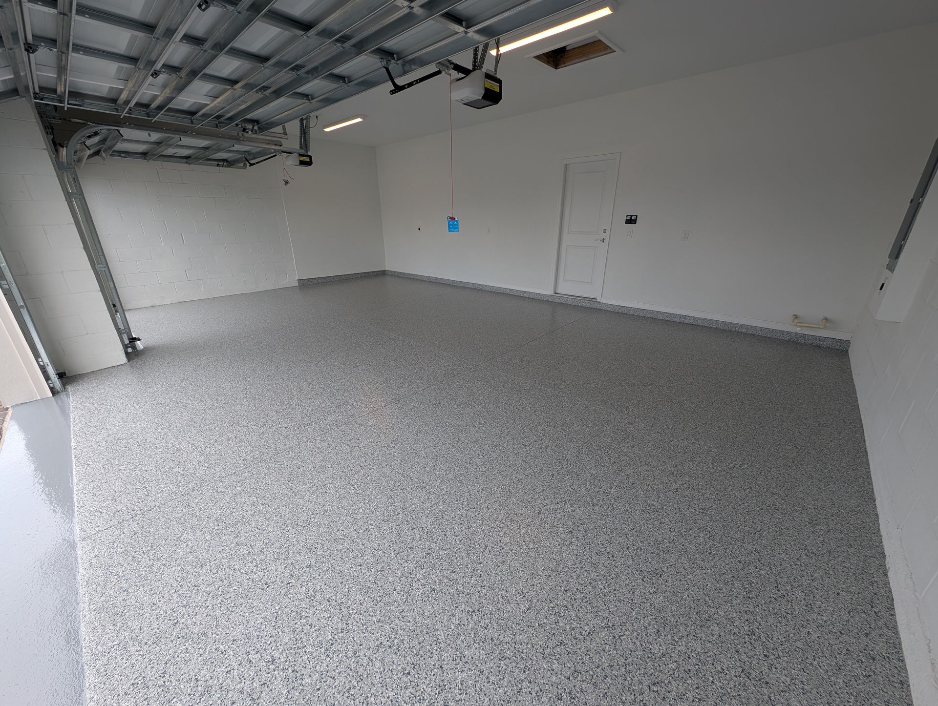 Empty garage with gray speckled floor, white walls, and exposed ceiling framing