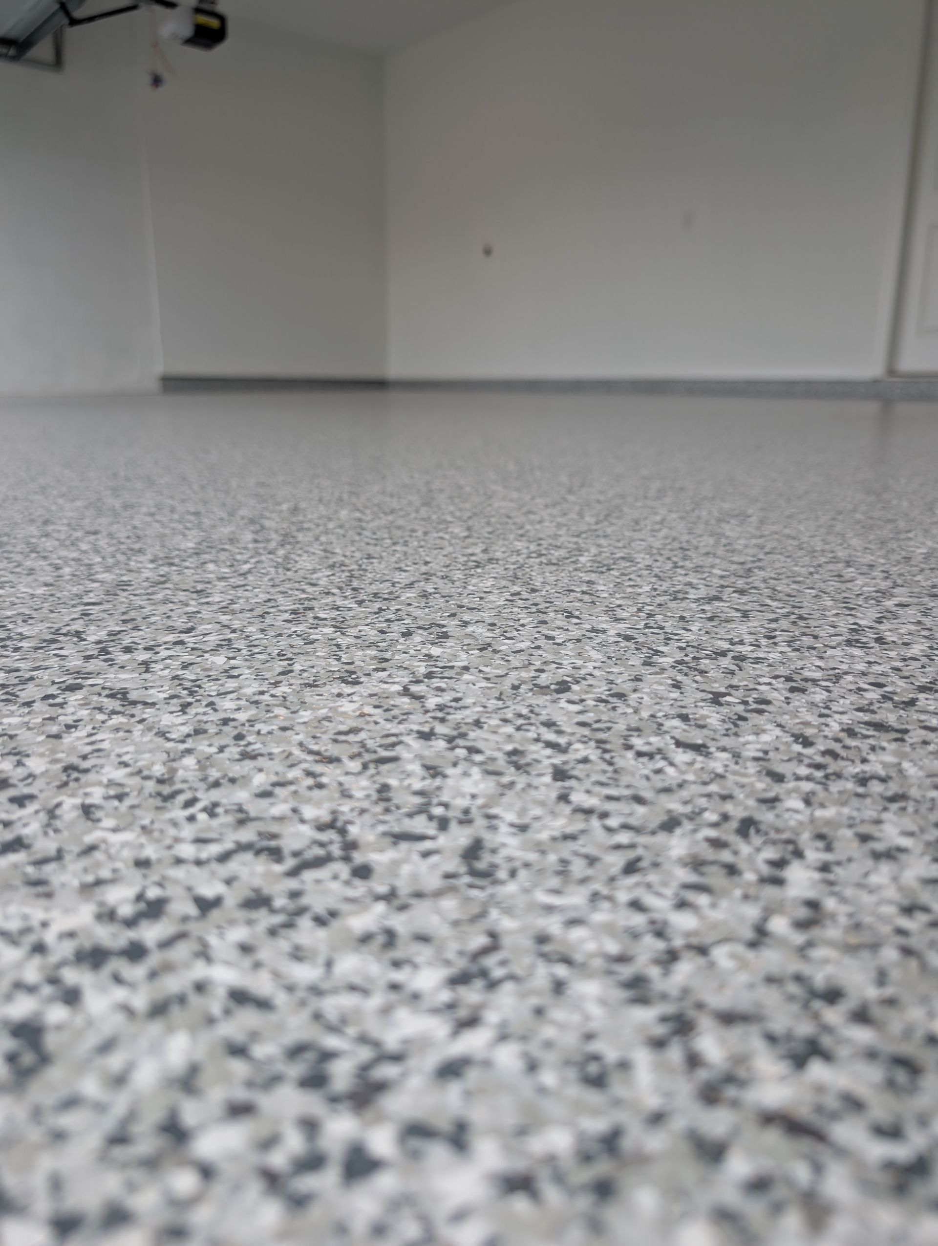 Empty room with speckled gray floor and white walls, viewed from low angle.