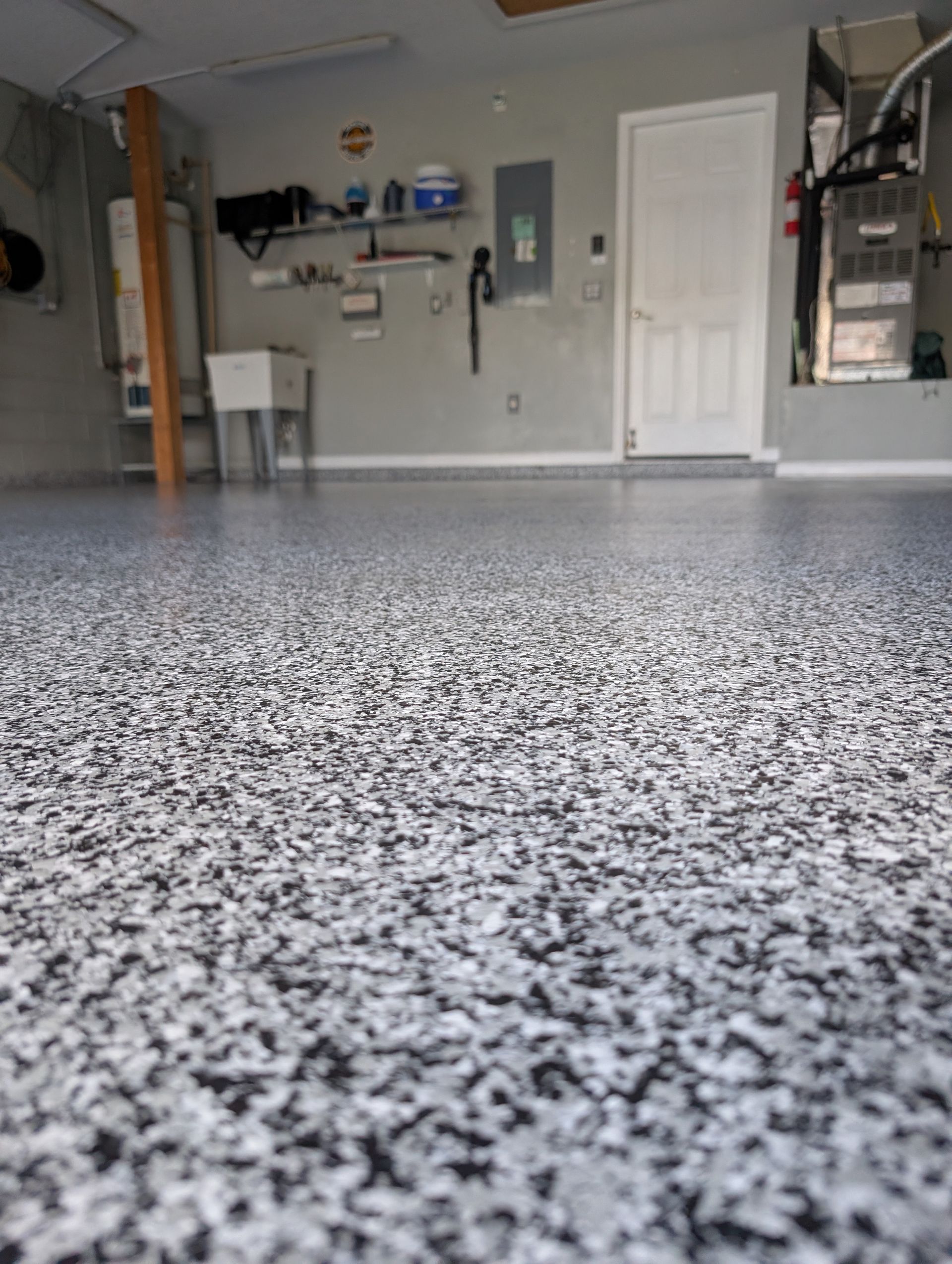 Empty garage with speckled epoxy floor, shelves on the back wall, and a white door.
