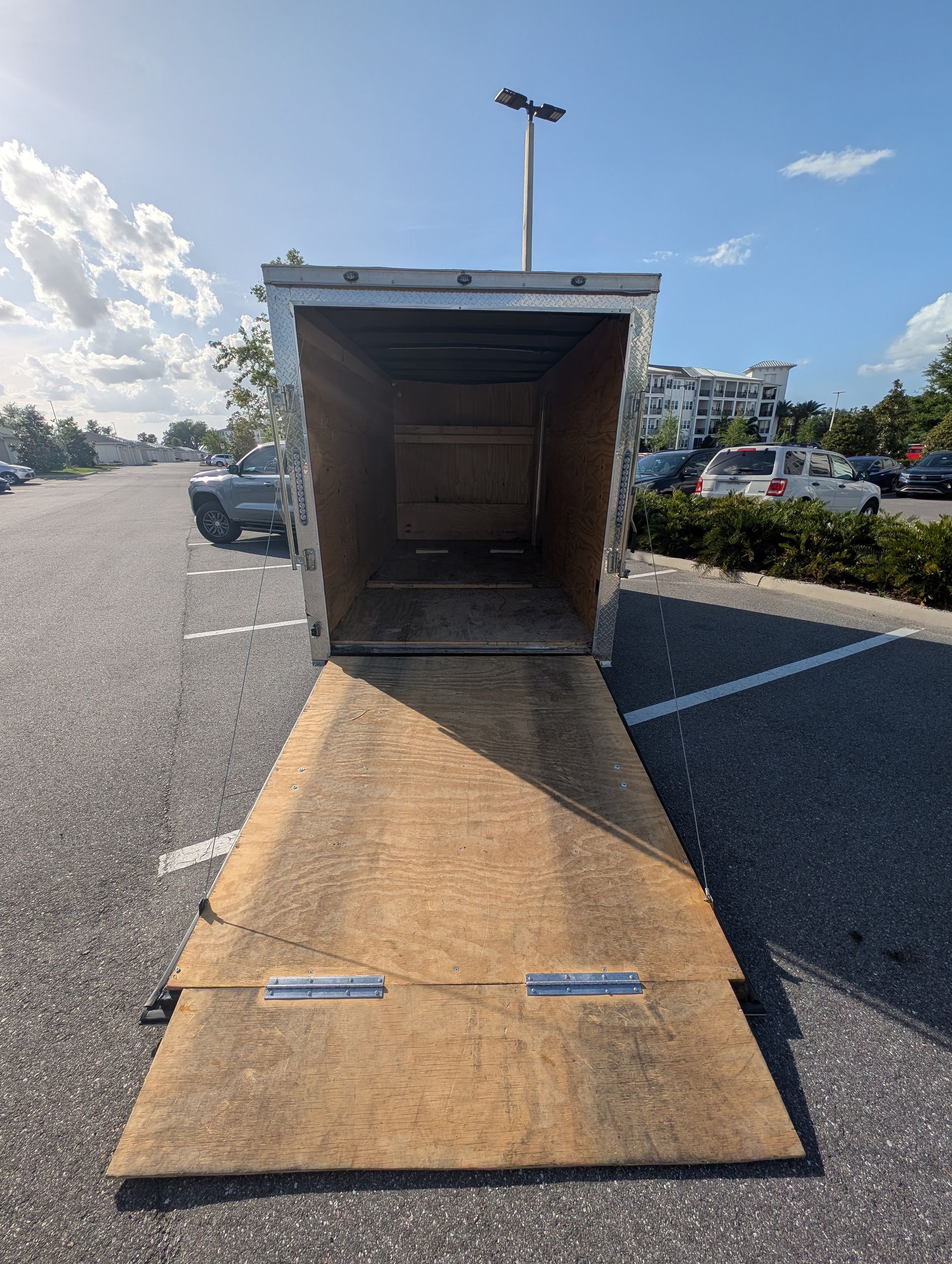 Open trailer with lowered ramp in a parking lot on a sunny day