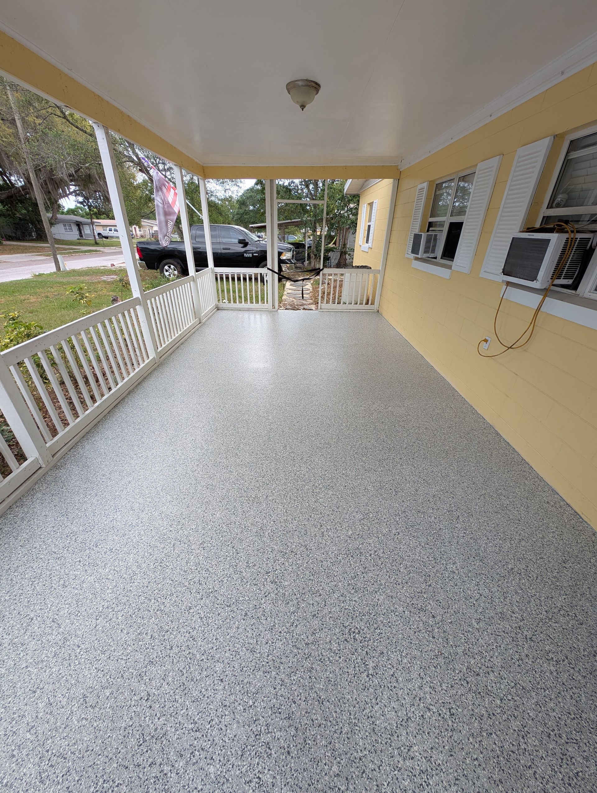 Covered front porch with white railing, speckled gray floor, yellow walls, and a view of the yard.