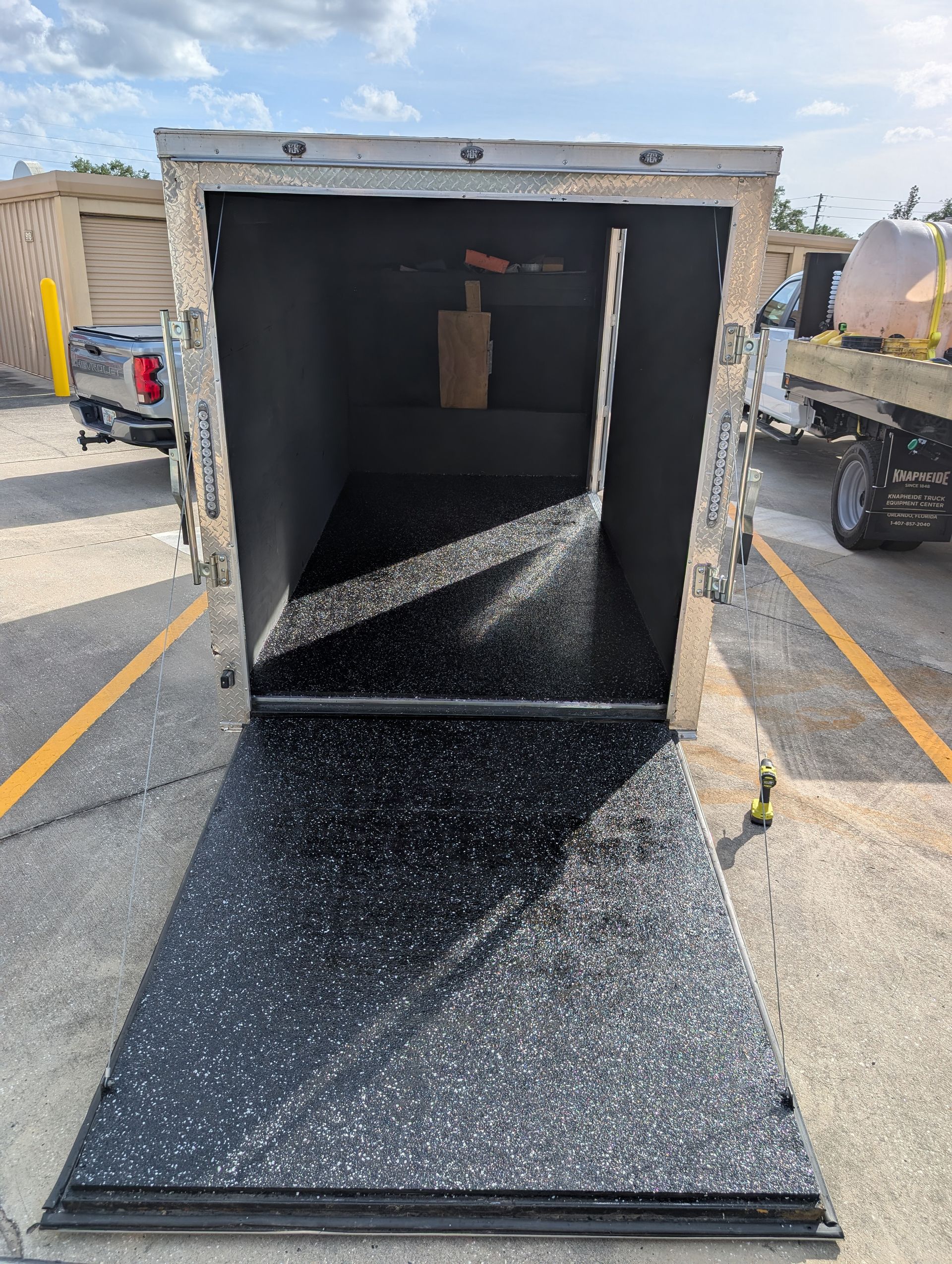 Open black cargo container with a ramp extending onto a parking lot, lit by daylight.