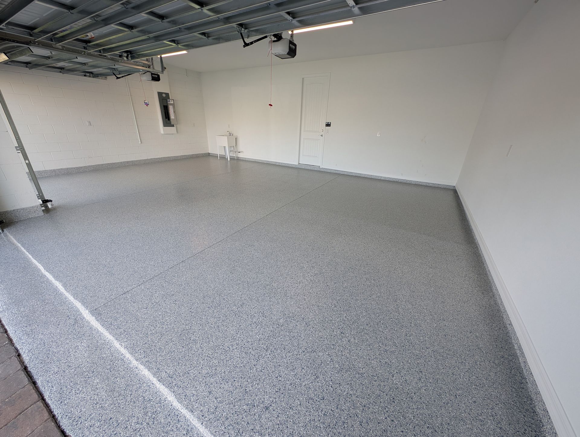 Empty unfinished garage with speckled epoxy floor, white walls, and exposed ceiling fixtures