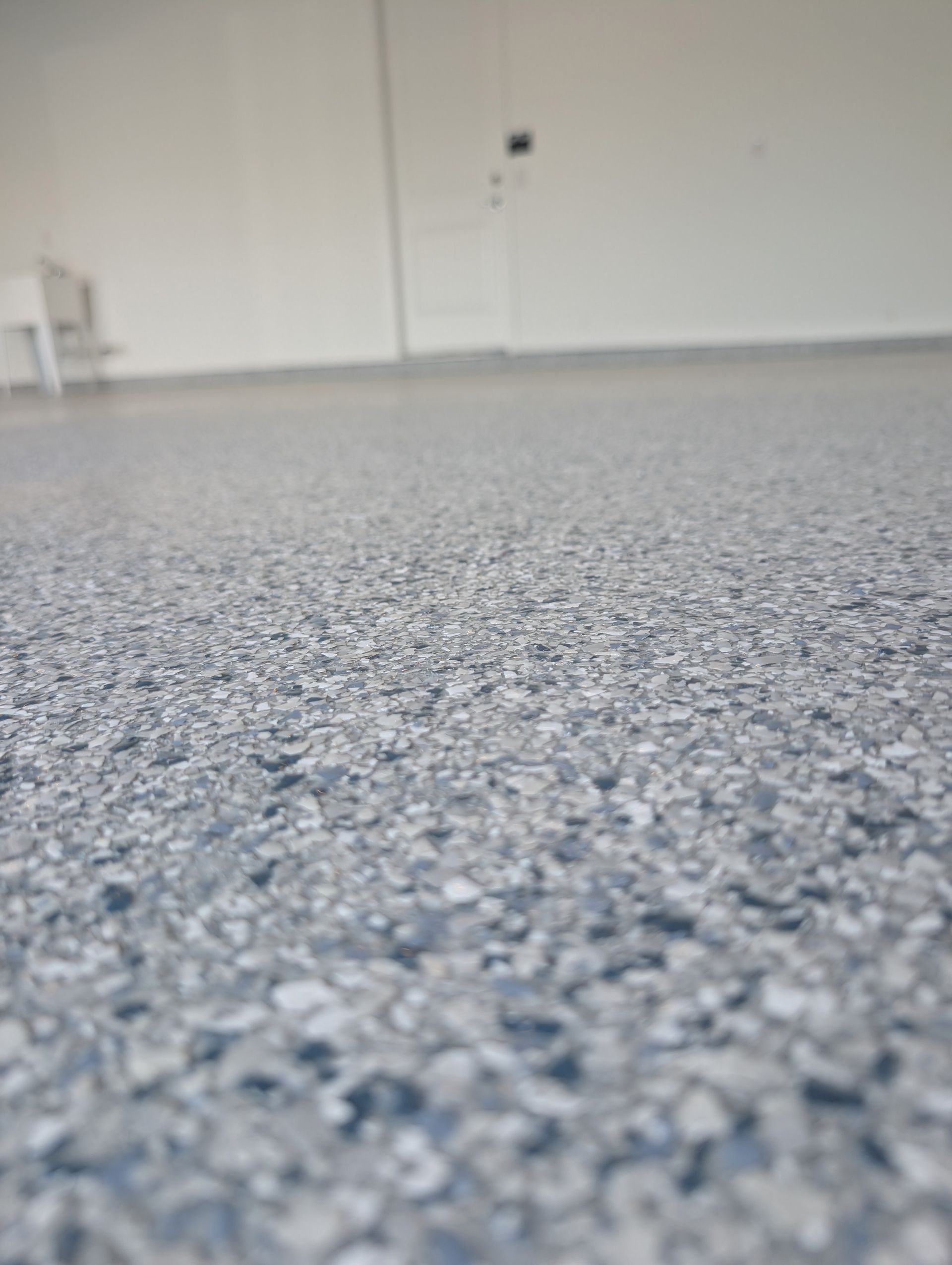 Low-angle view of a speckled blue-gray floor in an empty white room