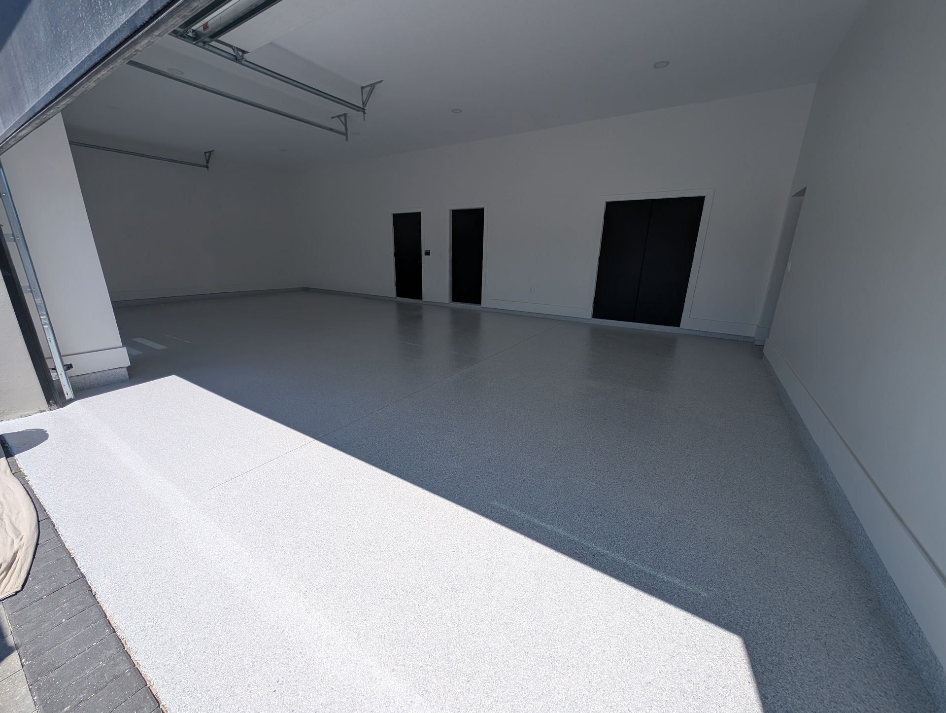 Empty white garage or warehouse interior with gray floor and dark doors.