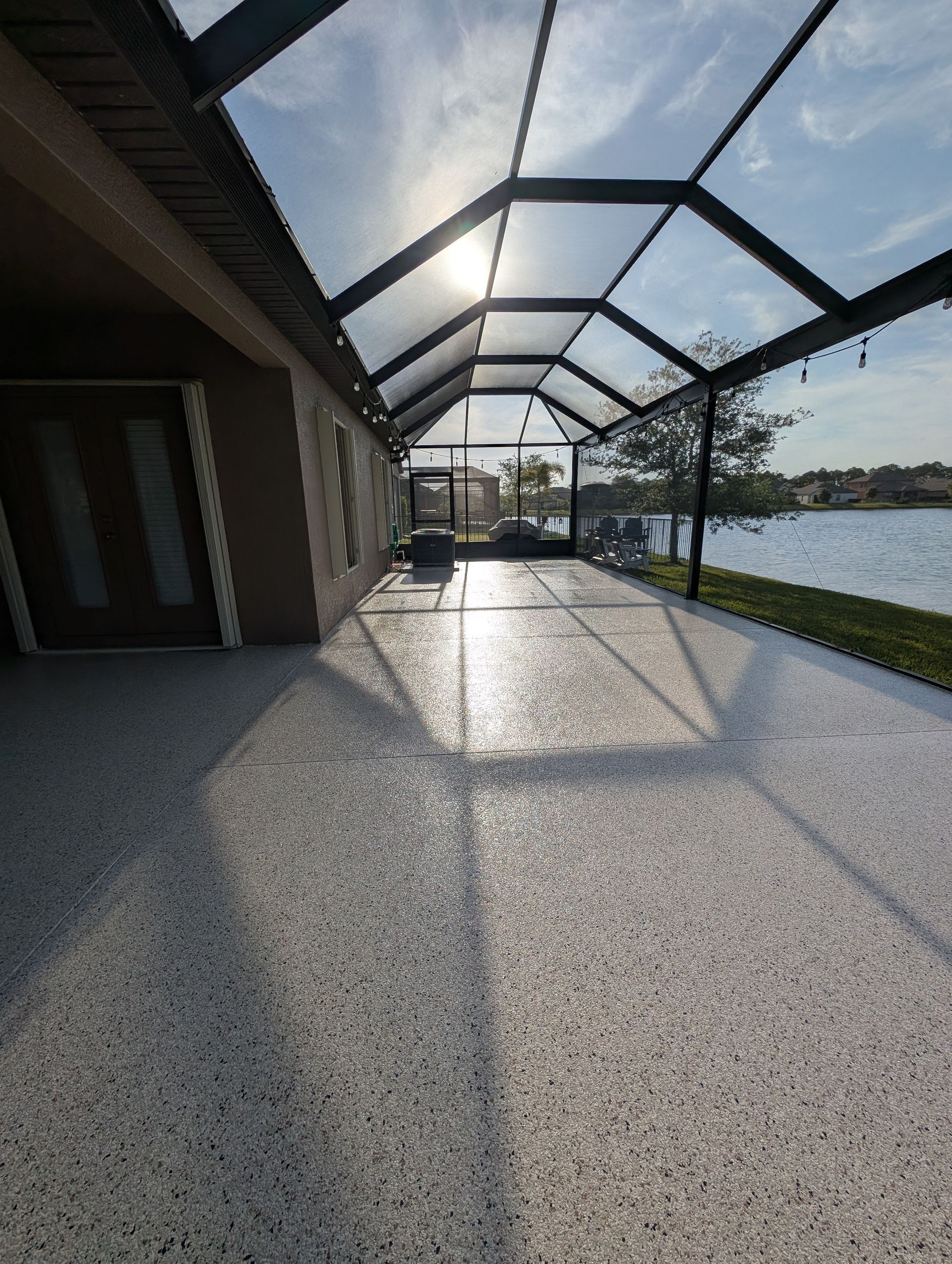 Sunlit covered patio with glass roof beside a river, casting long shadows on the floor
