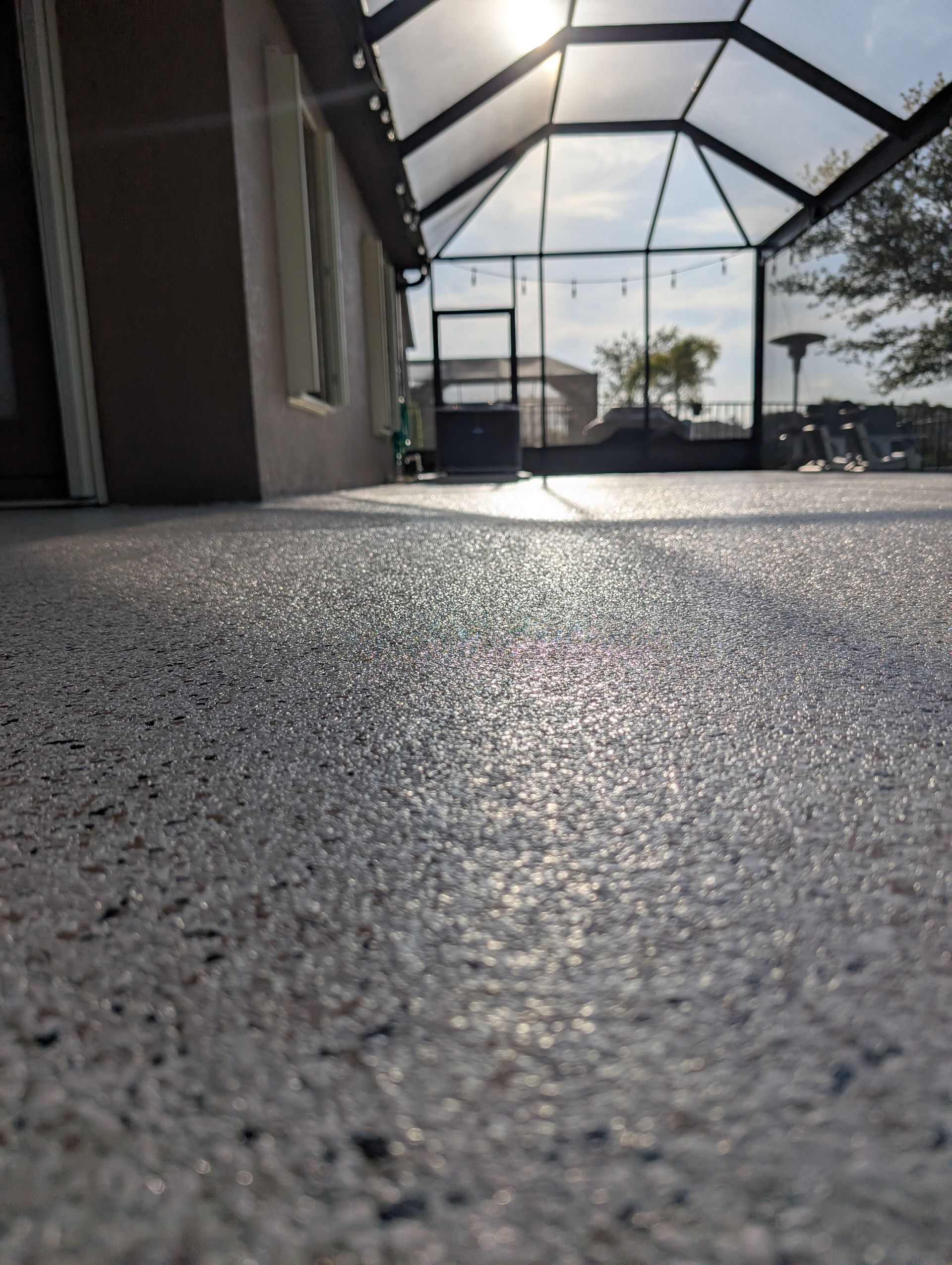 Low-angle view of a sunlit screened patio floor and enclosure with house wall on the left.