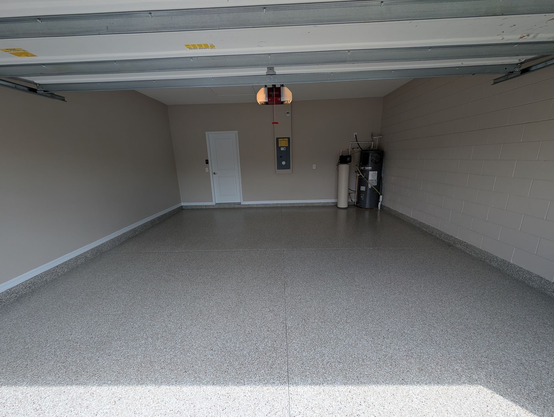 Empty garage with speckled gray floor, beige walls, white door, and storage tank at the back.