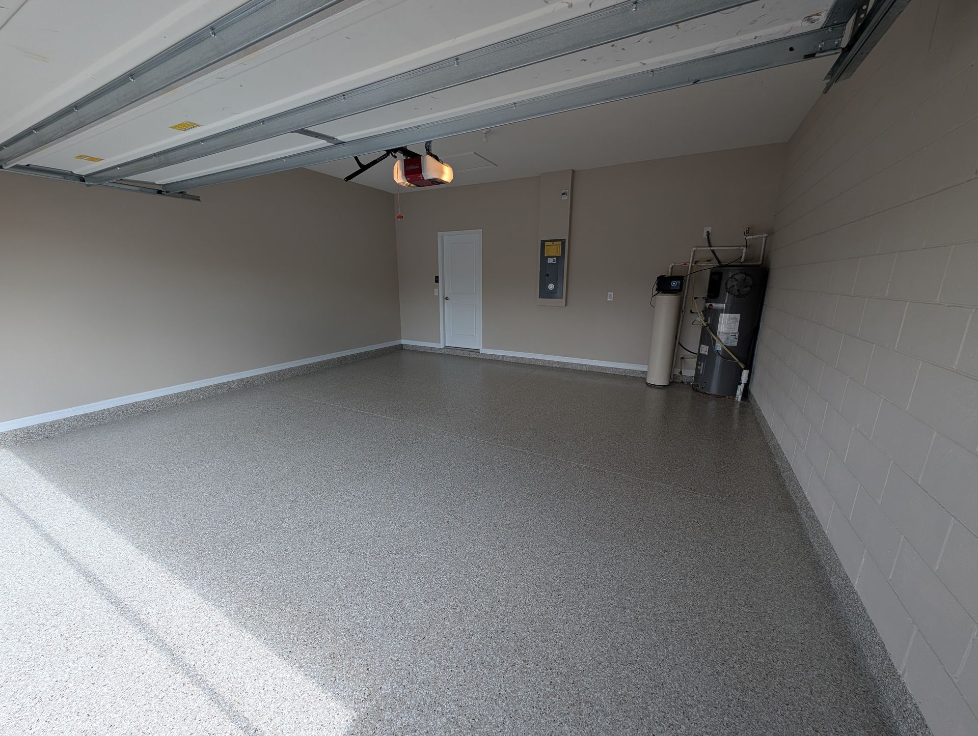 Empty garage with speckled epoxy floor, open overhead door, and water heater on the right wall