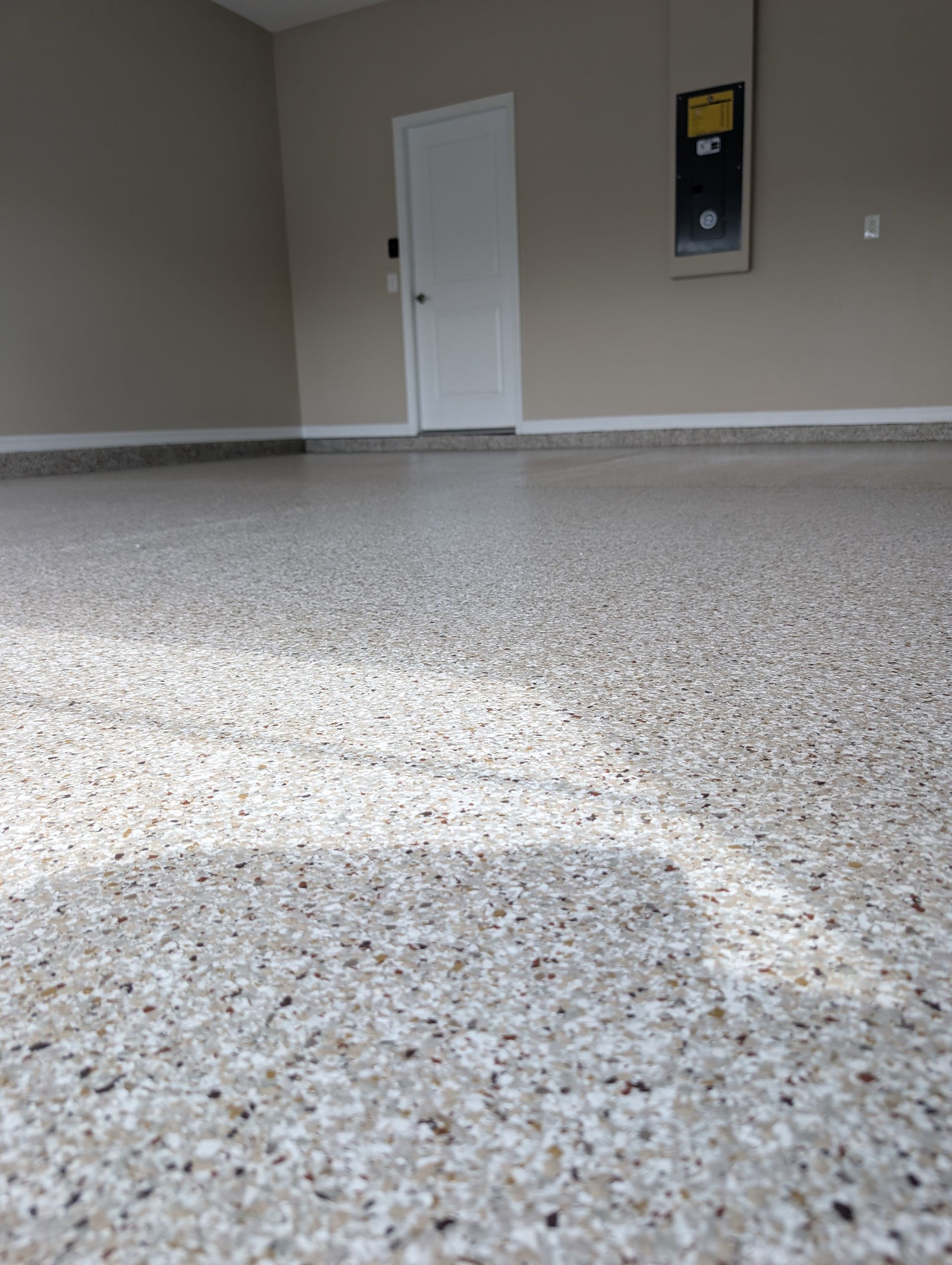 Empty garage with speckled concrete floor, gray walls, white door, and sunlight across the floor