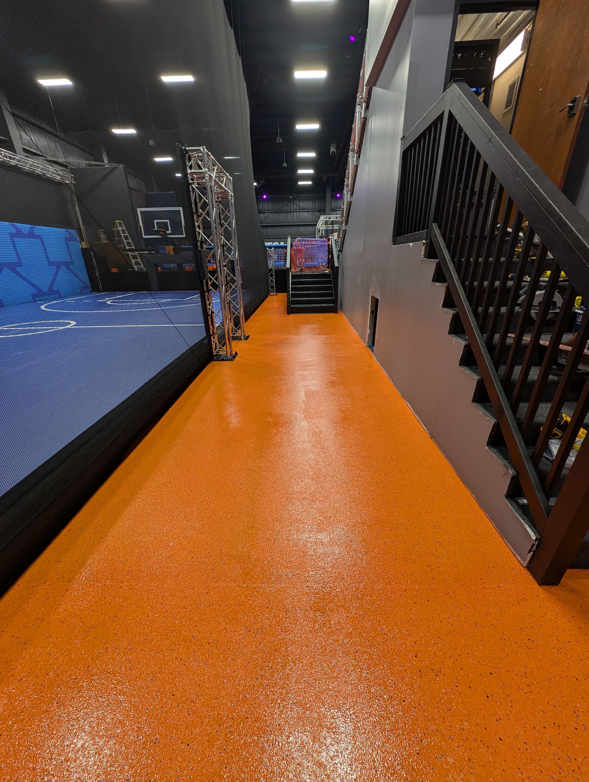 Orange indoor walkway with black railings and overhead lights, leading toward a seating area.