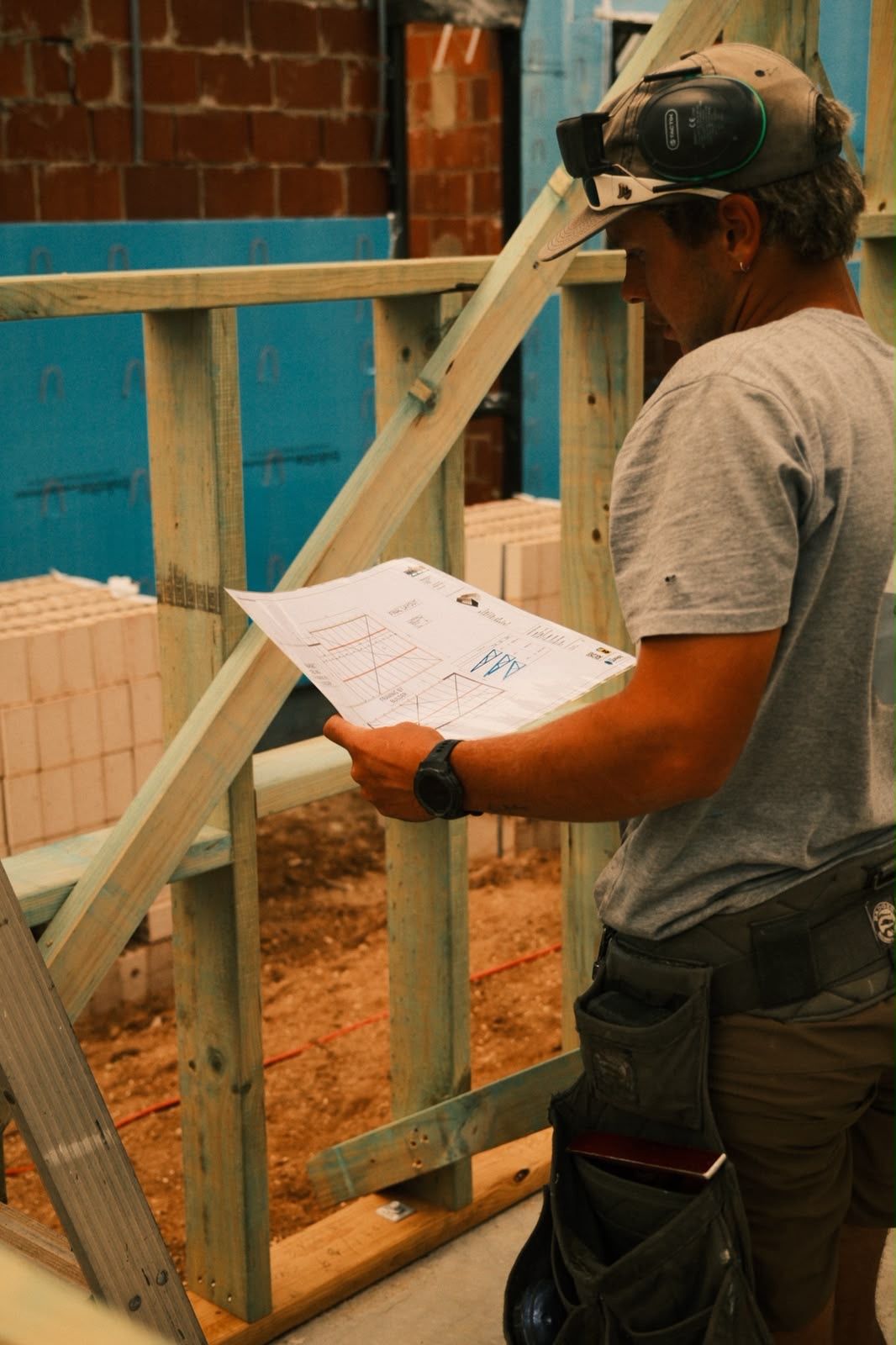 Worker wearing a headset reviews a clipboard at a construction site beside a wooden frame