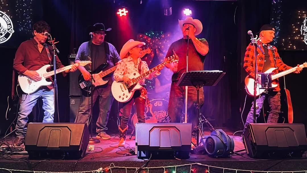 Country band performing onstage under red and purple lights, with guitars, fiddle, and microphones.