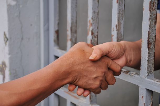 Hands shaking through jail bars, symbolizing a prison visit or reunion
