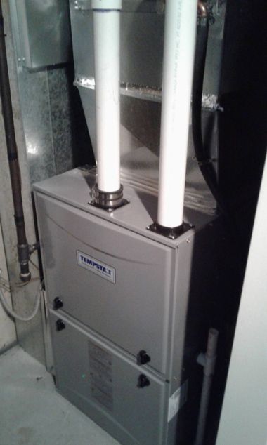 A gray Lennox furnace with two white PVC exhaust pipes extending from the top, located in a utility area.