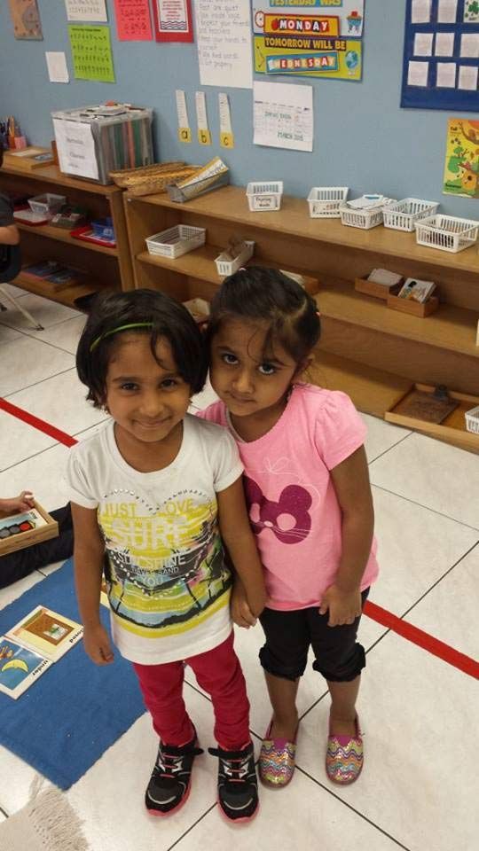 Two Little Girls Are Standing Next to Each Other in a Classroom