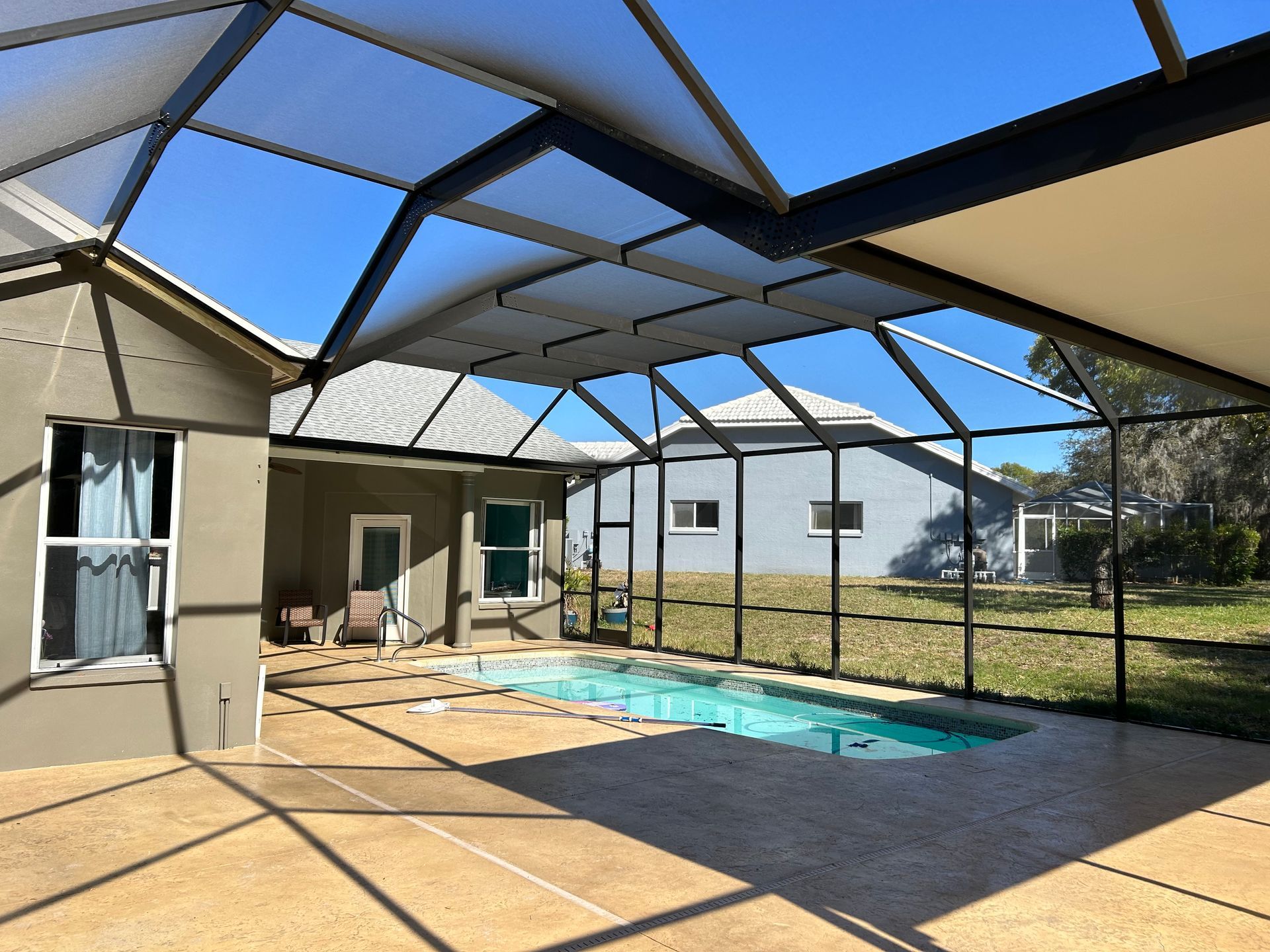 Pool area with screen enclosure, blue pool, tan patio, and clear sky.