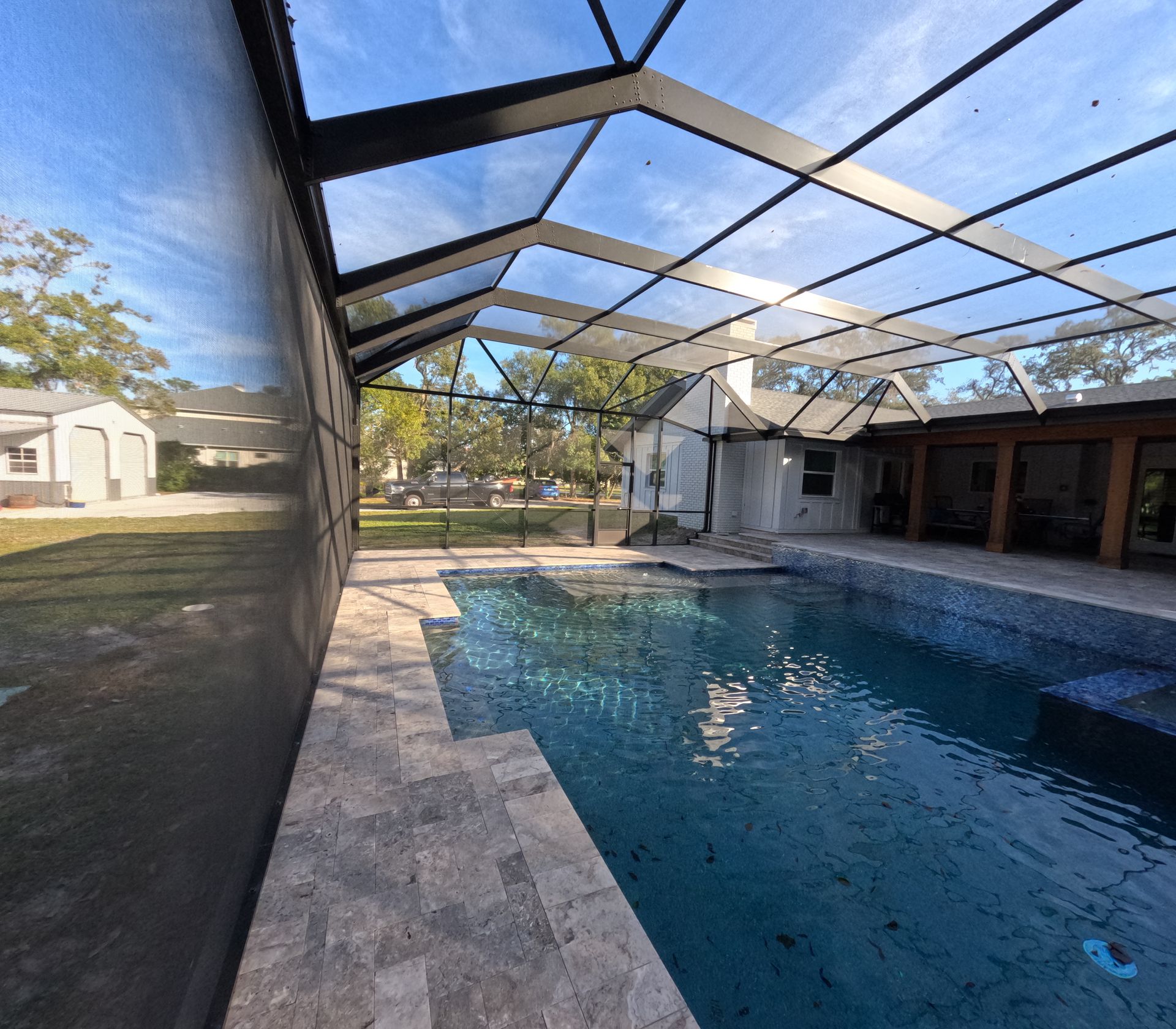 Pool under a screened enclosure with a stone deck, blue water, and a sunny sky.