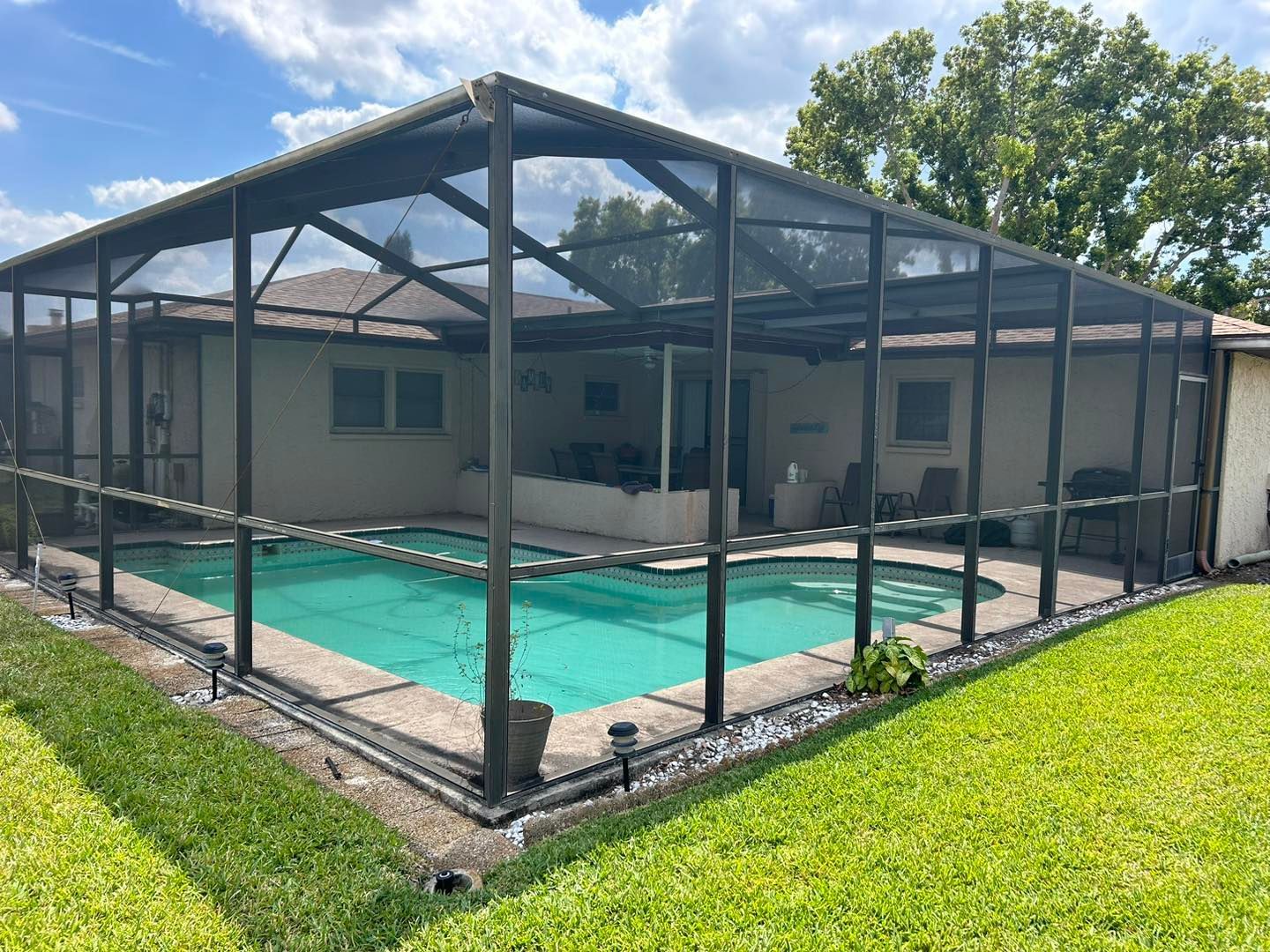Screened-in pool enclosure with a turquoise pool, surrounded by concrete and green grass.