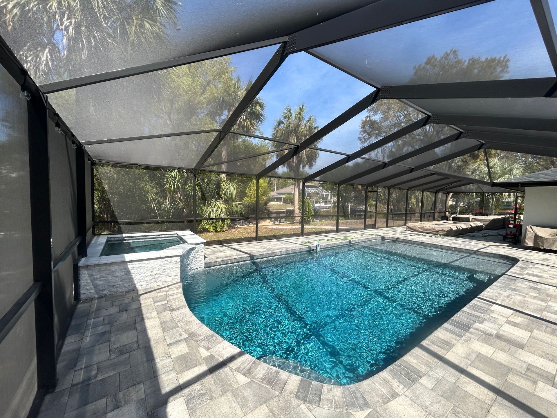 Pool and spa enclosed by a screened patio with blue water and stone patio, sunny day.
