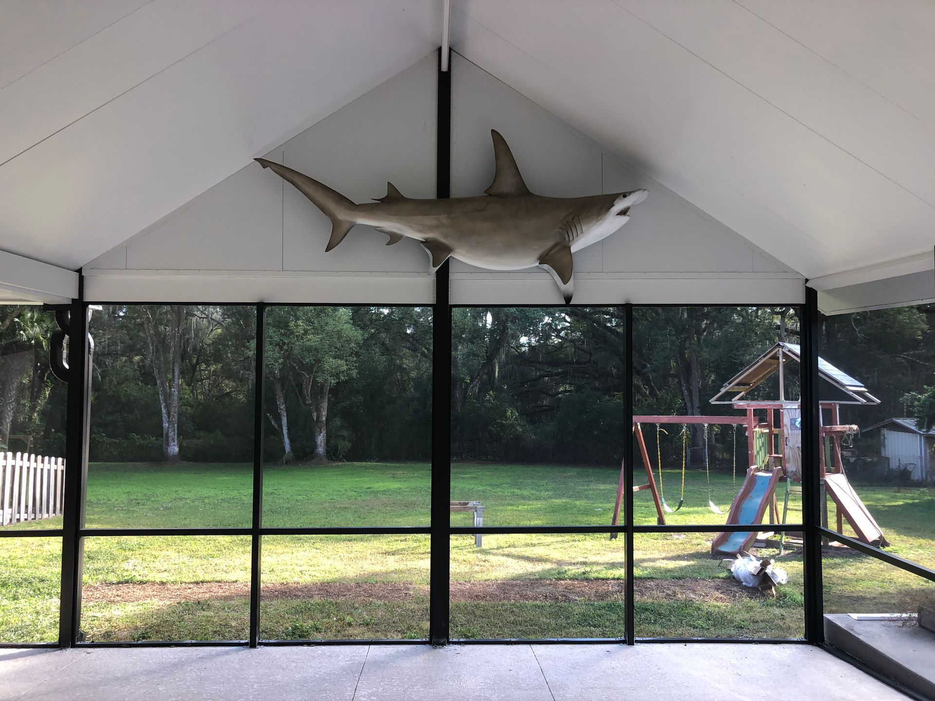 Screened porch with mounted shark, overlooking a backyard with a swing set.