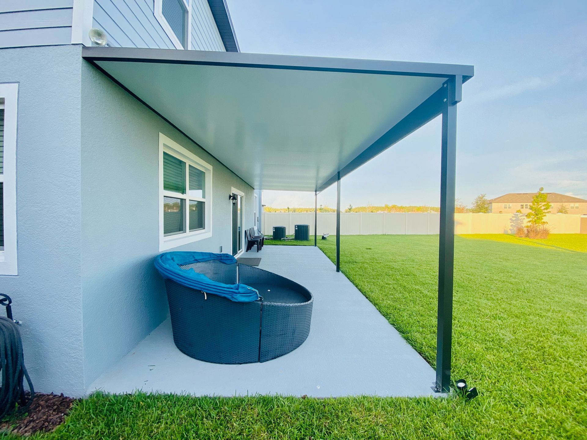 A covered patio with a gray concrete floor, overlooking a grassy lawn. A rounded outdoor chair sits against the house.