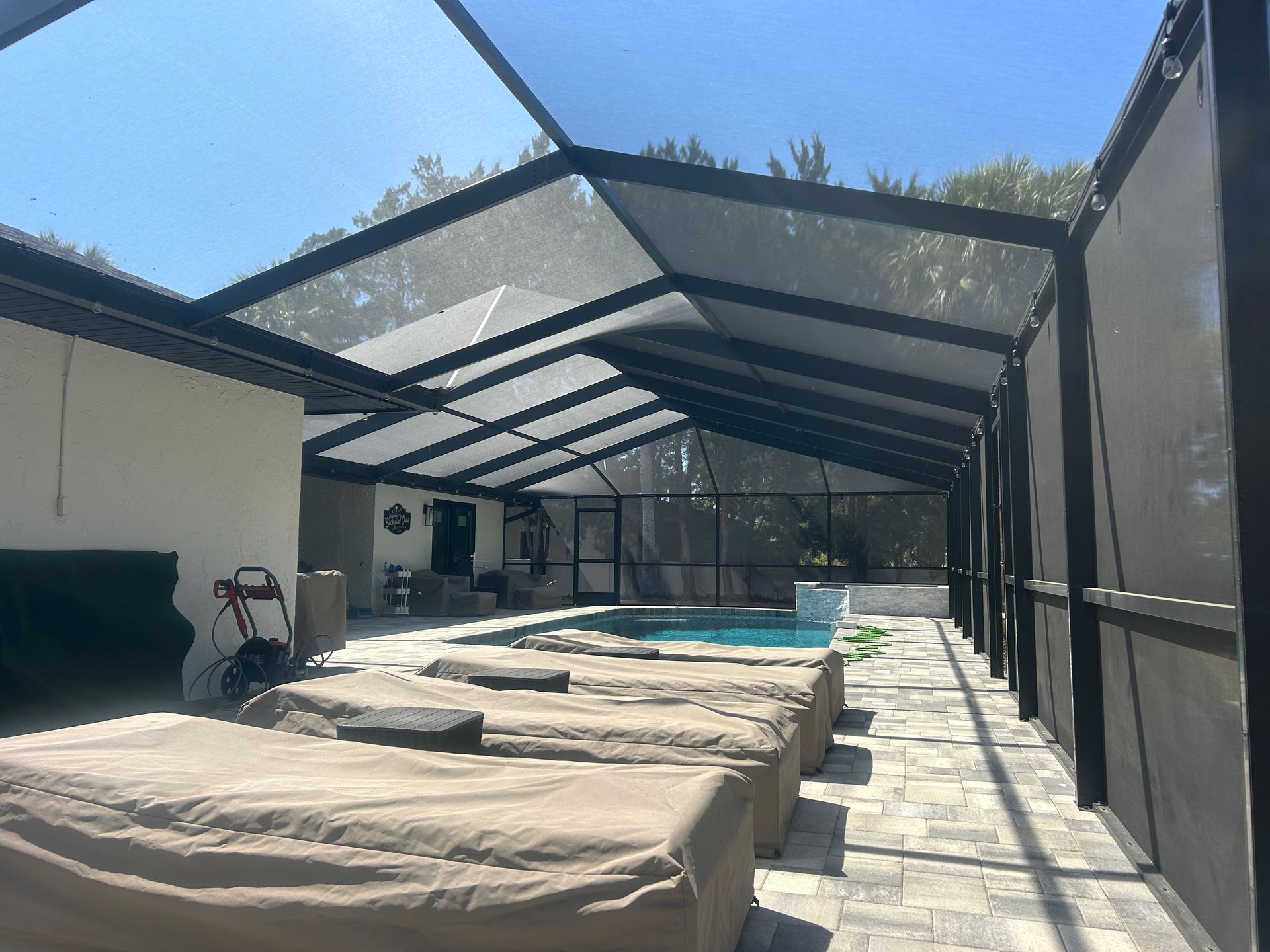 Poolside patio with screen enclosure, covered lounge chairs, and blue pool under a sunny sky.